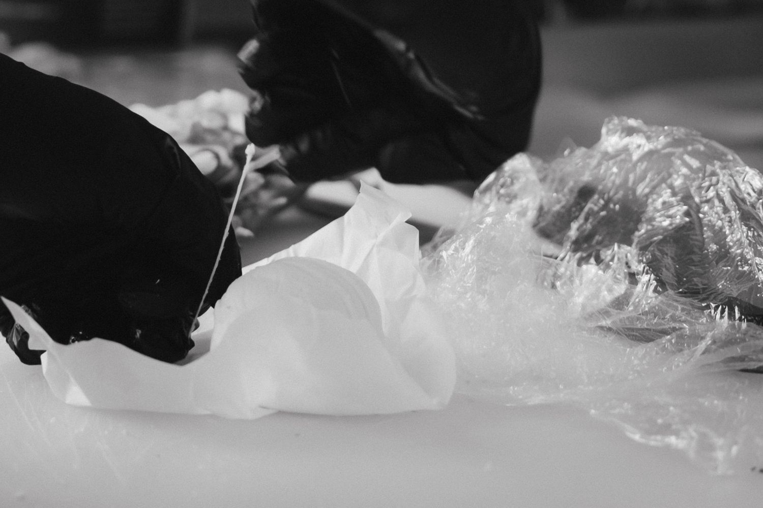Black and white close-up of gloved hands working with white plastic material on a surface.