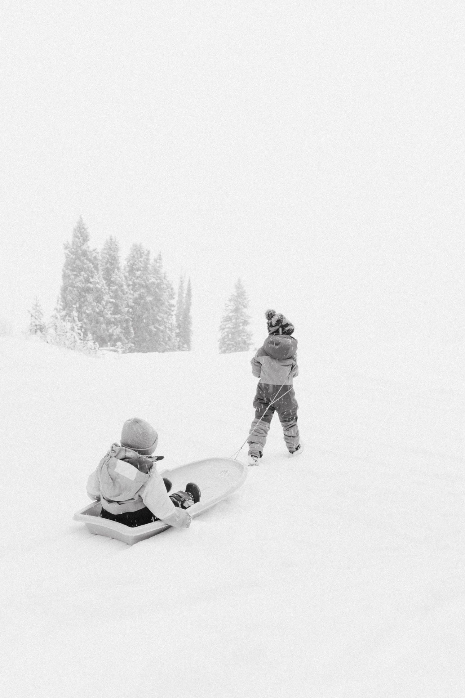 Four black and white winter scenes show people playing and sledding in deep snow on a snowy hillside.