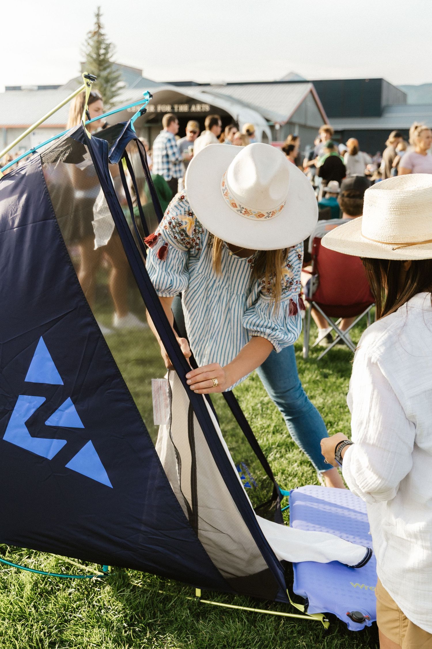 People setting up outdoor event tents and equipment on grassy lawn with a blue and black flag visible.