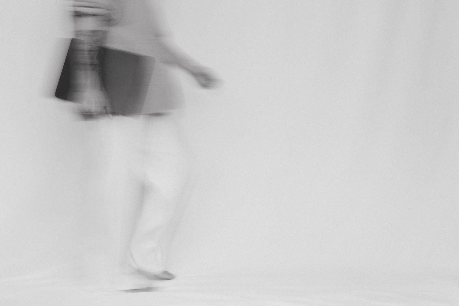 Blurred black and white photo of a person walking while carrying a shopping bag, captured with motion blur effect.