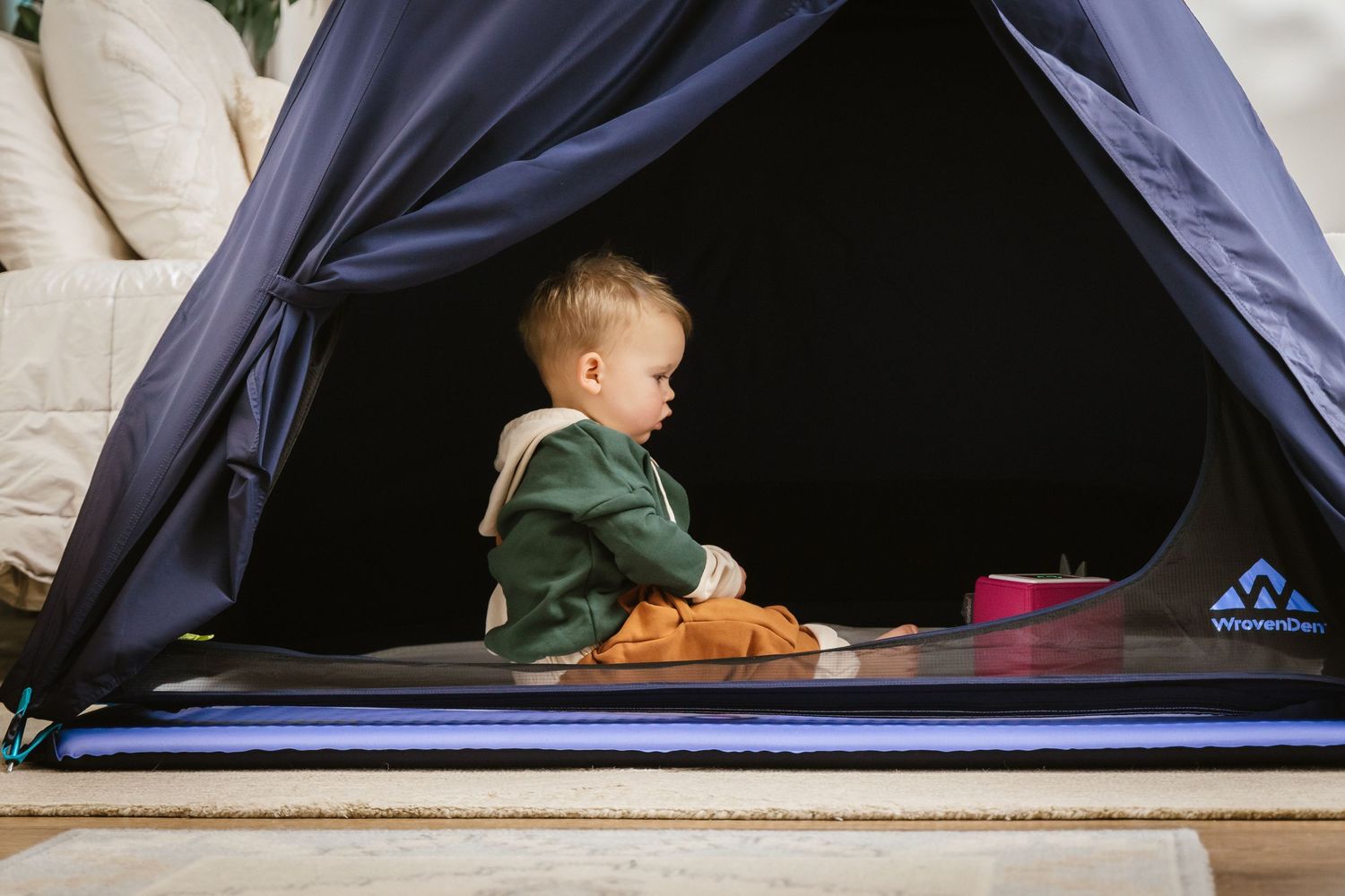 A child plays inside a dark blue tent while camping outdoors on a sunny day.