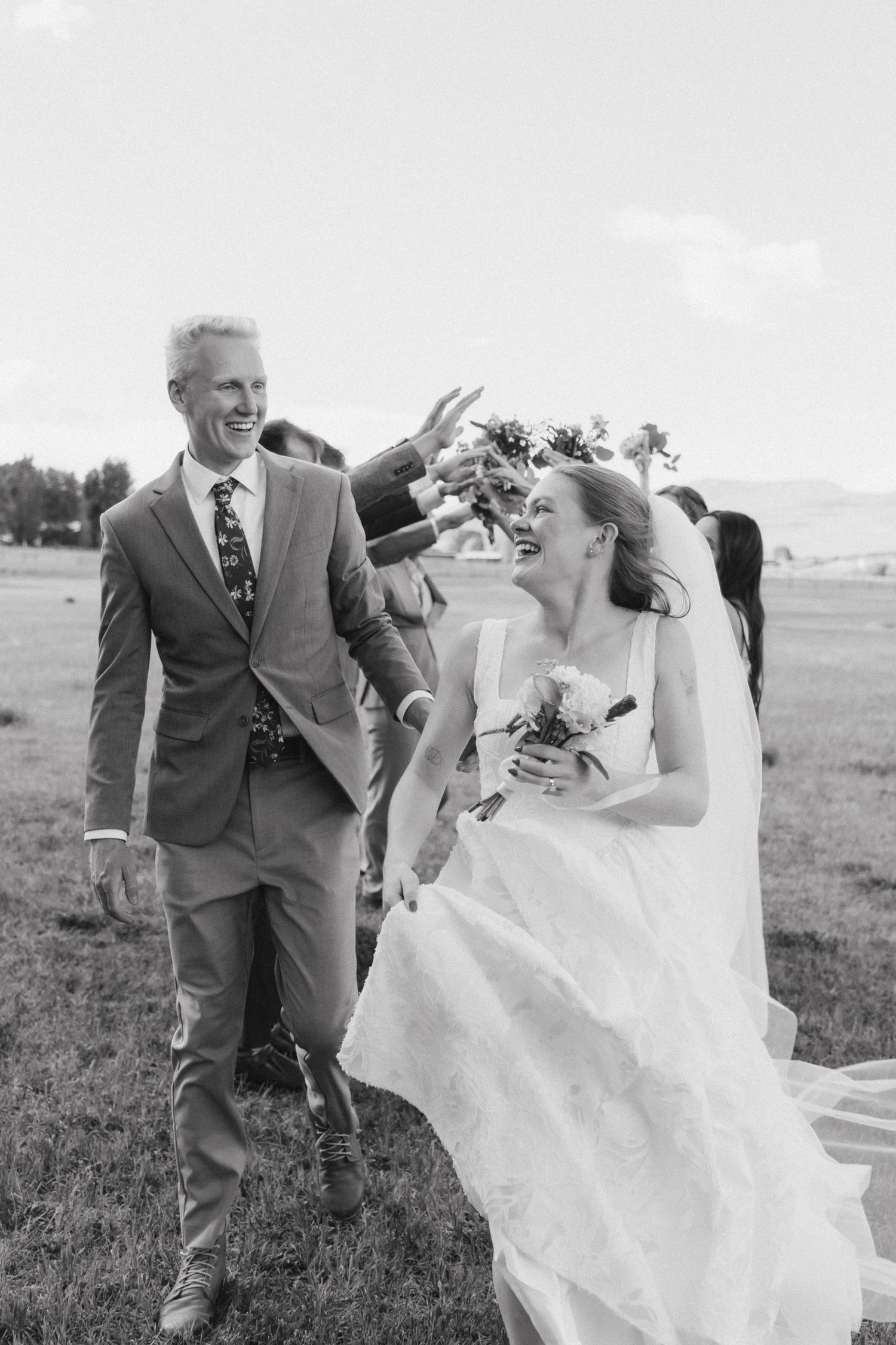 Black and white photo of a laughing bride and groom walking outdoors at their wedding ceremony.