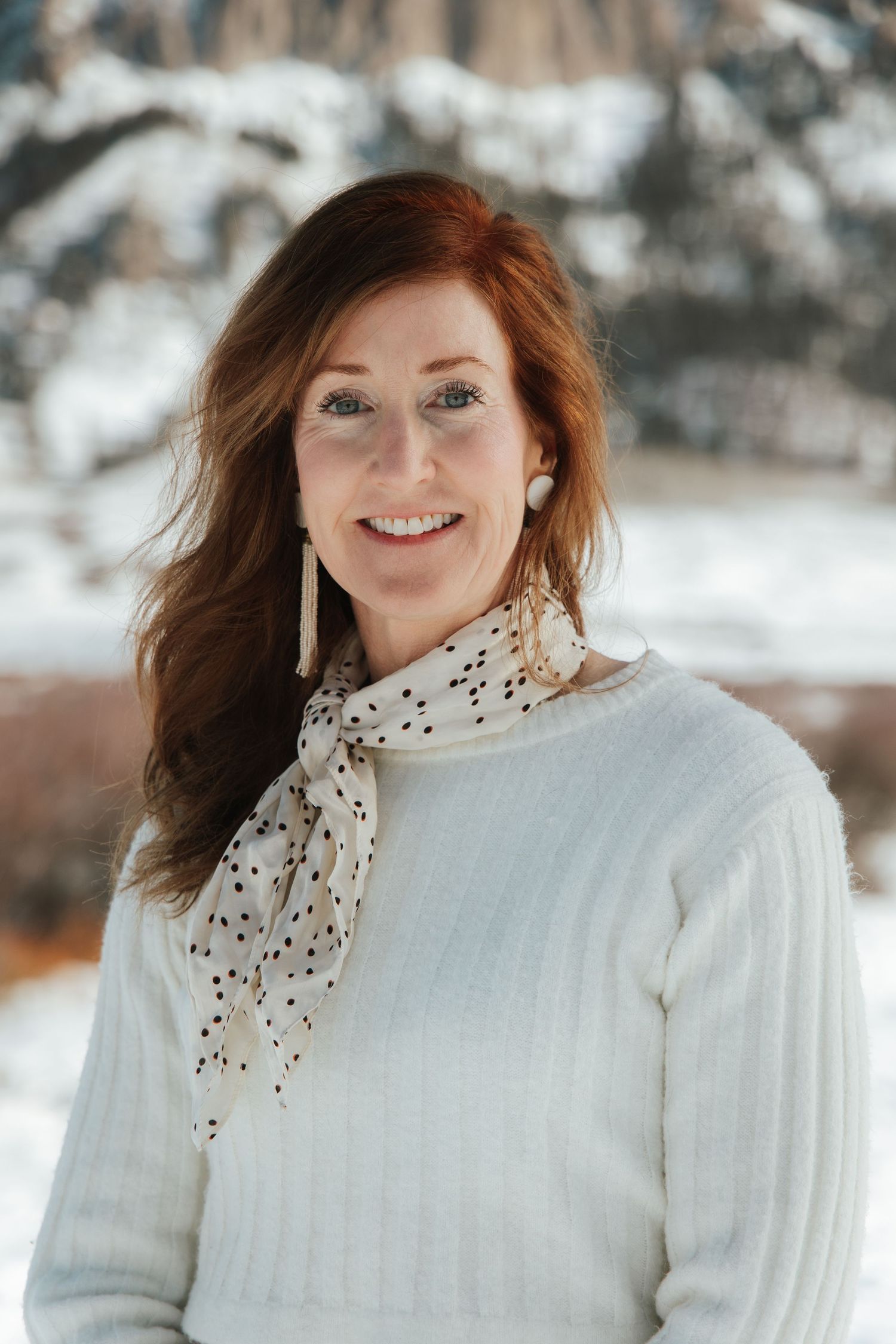 Person wearing a white sweater and polka dot scarf poses outdoors in a snowy winter setting.