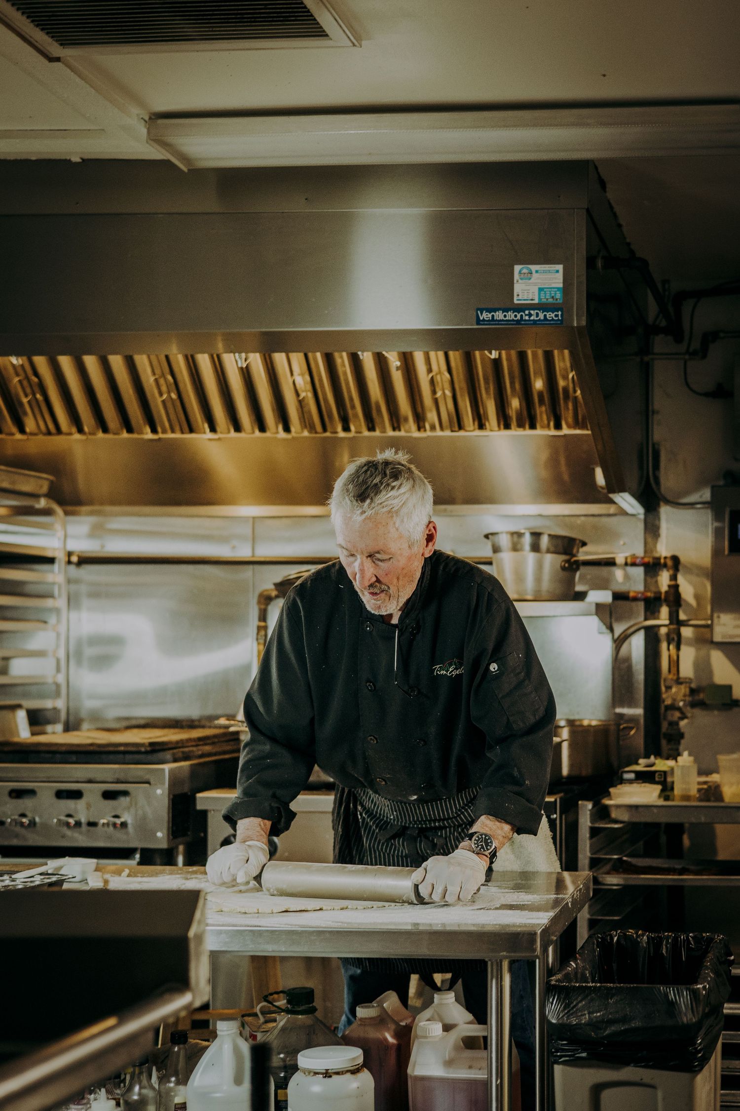 Chef in black uniform works diligently at stainless steel prep station in professional restaurant kitchen.
