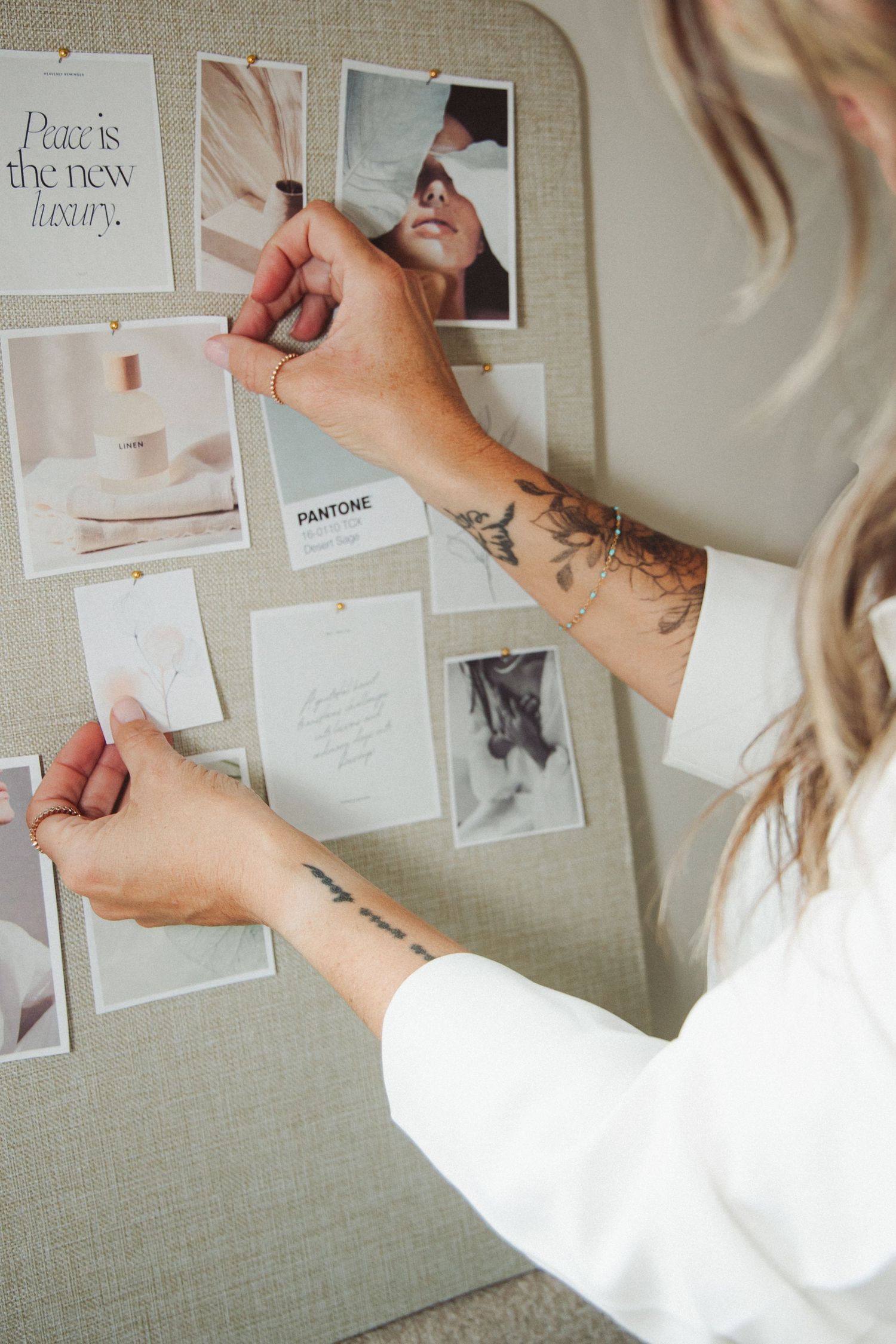Woman with tattoos pinning photos and cards to a neutral toned mood board.