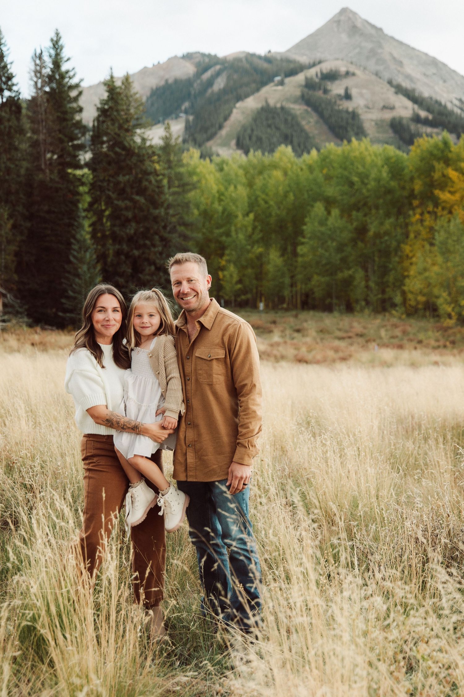 A scenic family portrait in tall grass with mountain peaks and autumn trees in the background. Crested Butte