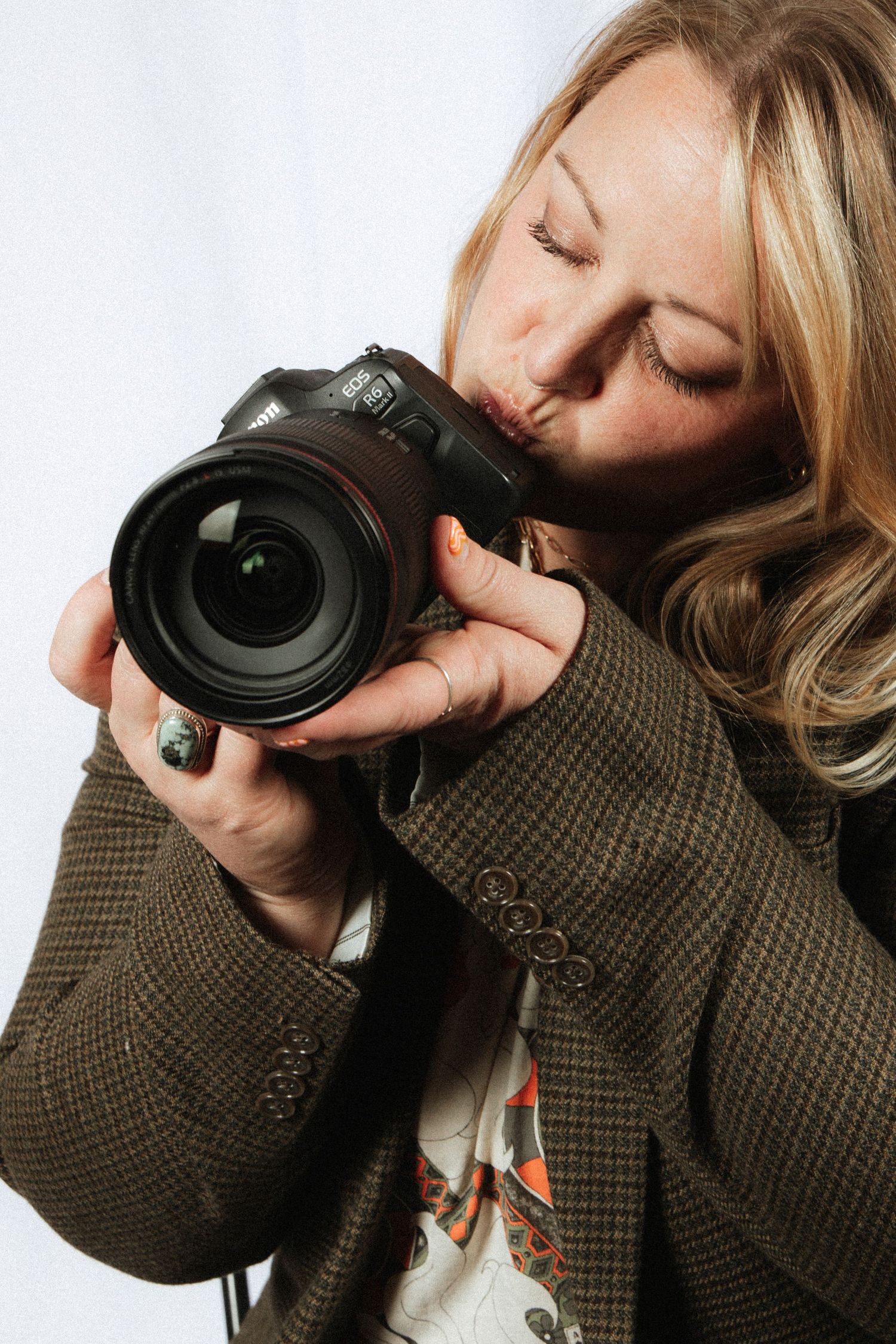 Photographer in brown tweed blazer holds professional DSLR camera while taking pictures against white background.