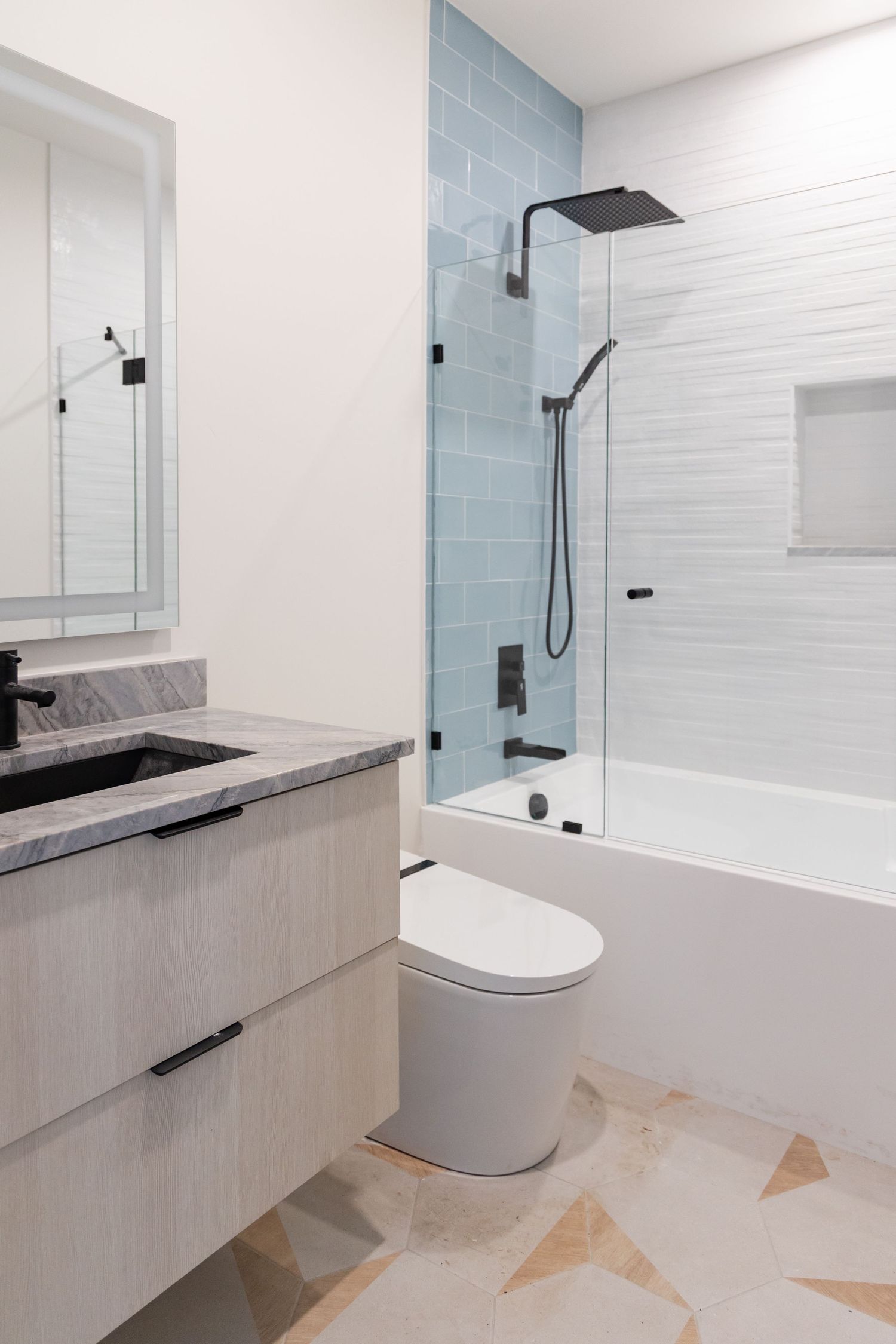 Modern bathroom with floating vanity, marble countertop, black fixtures, blue subway tile shower, and geometric patterned floor.