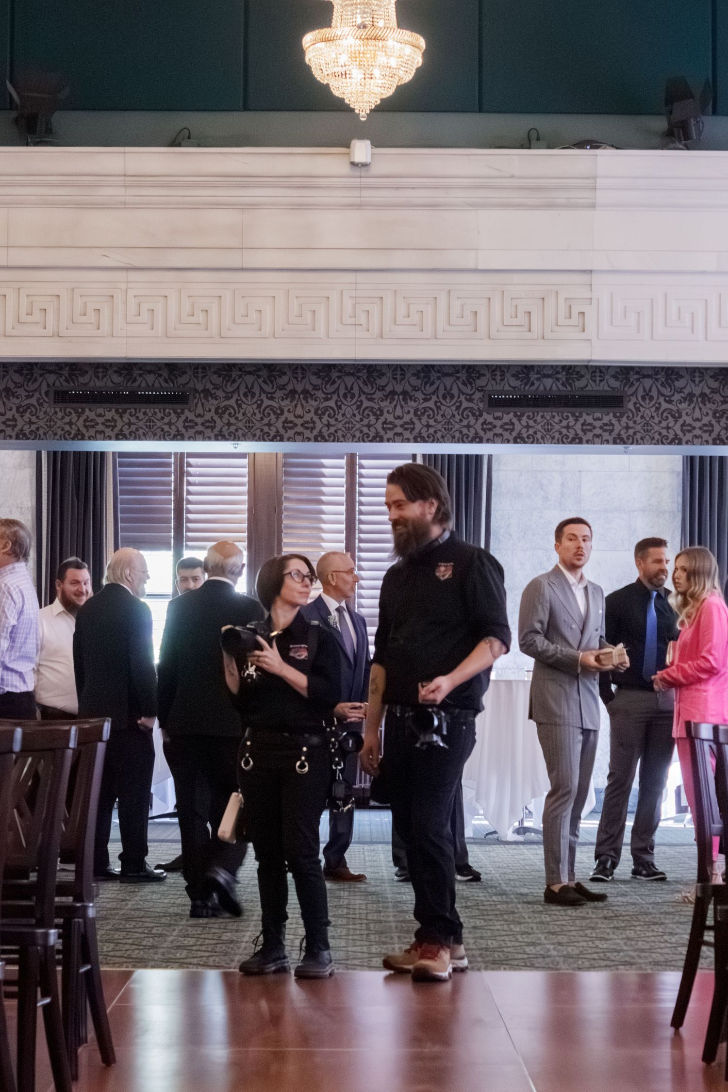 Wedding guests and venue staff gather in an elegant reception hall under a crystal chandelier.