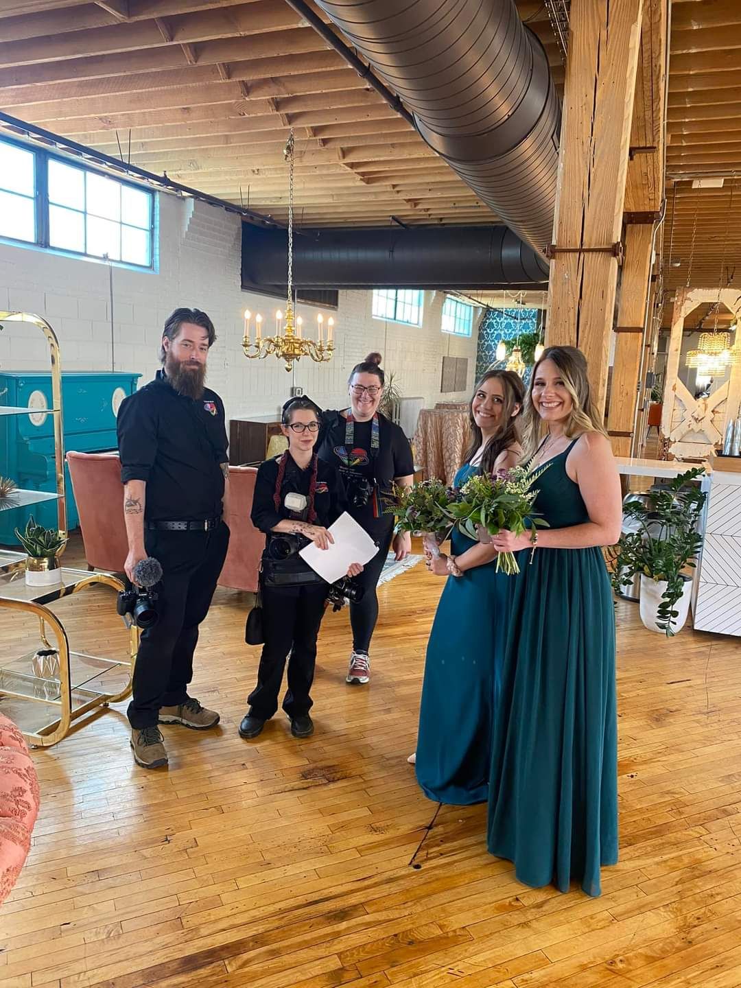 A group gathered in a rustic event space with wooden beams and elegant chandeliers.