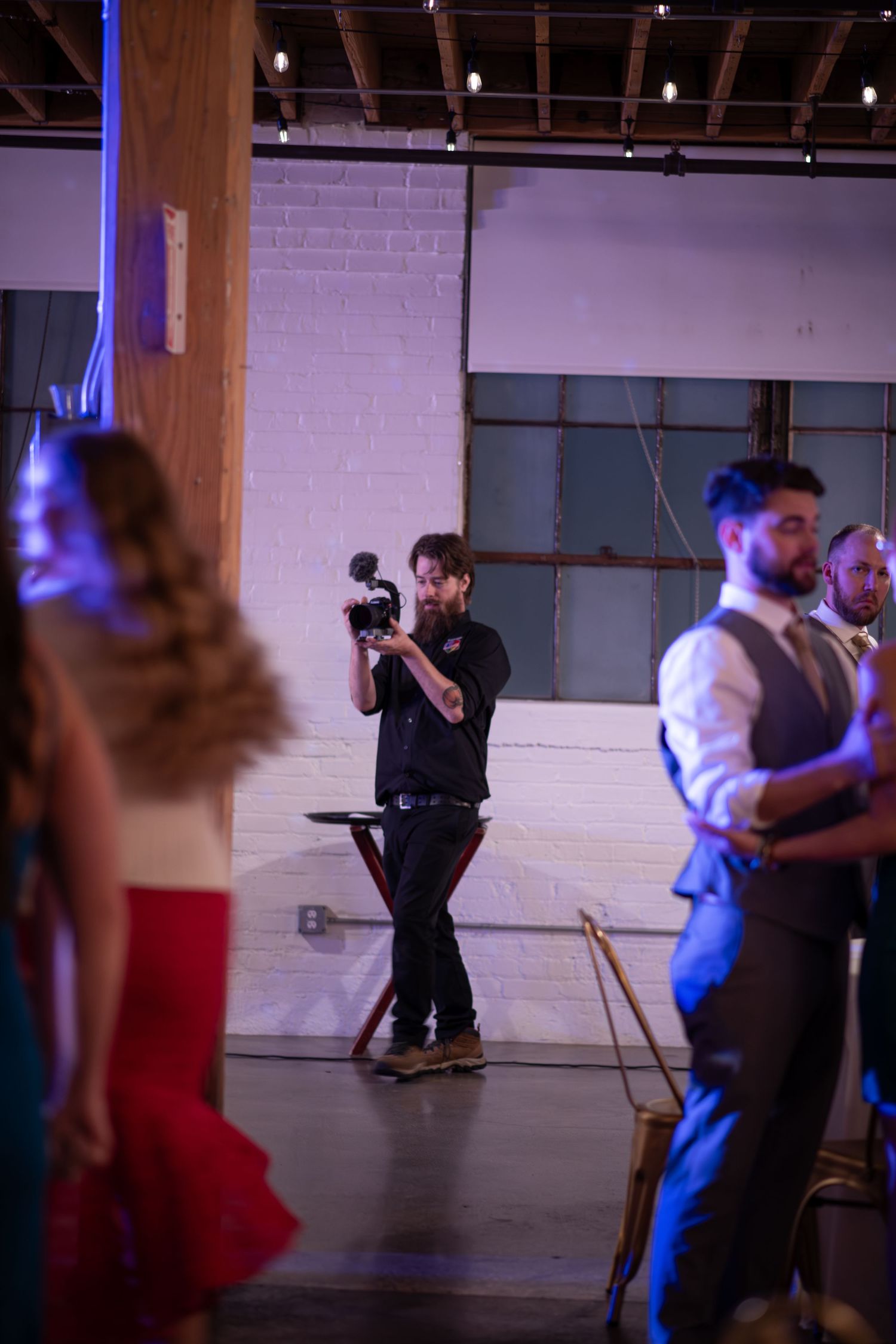 A photographer captures moments during a wedding reception in an industrial venue.