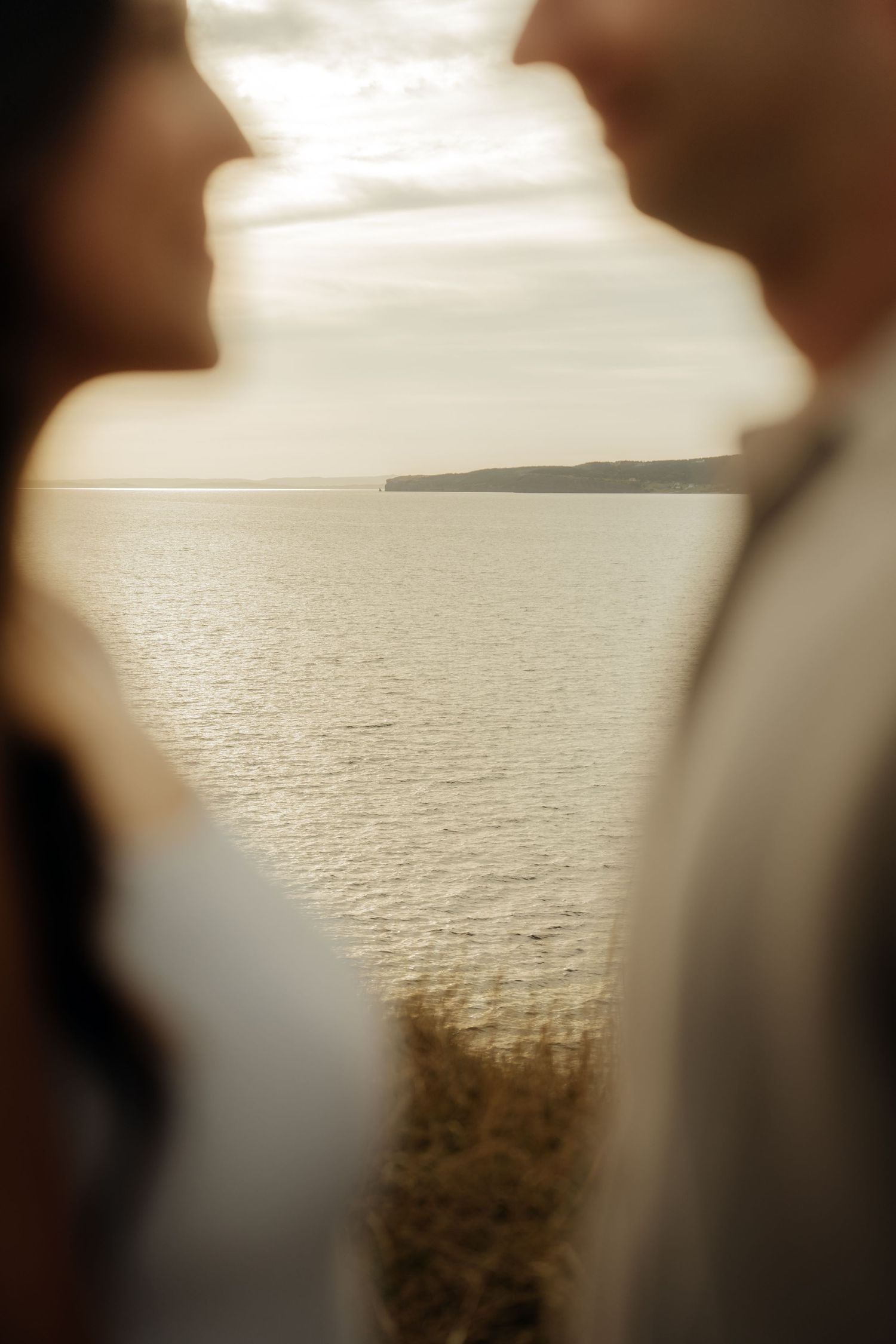 Romantic silhouettes stand against a golden ocean horizon at sunset creating a dreamy atmosphere.