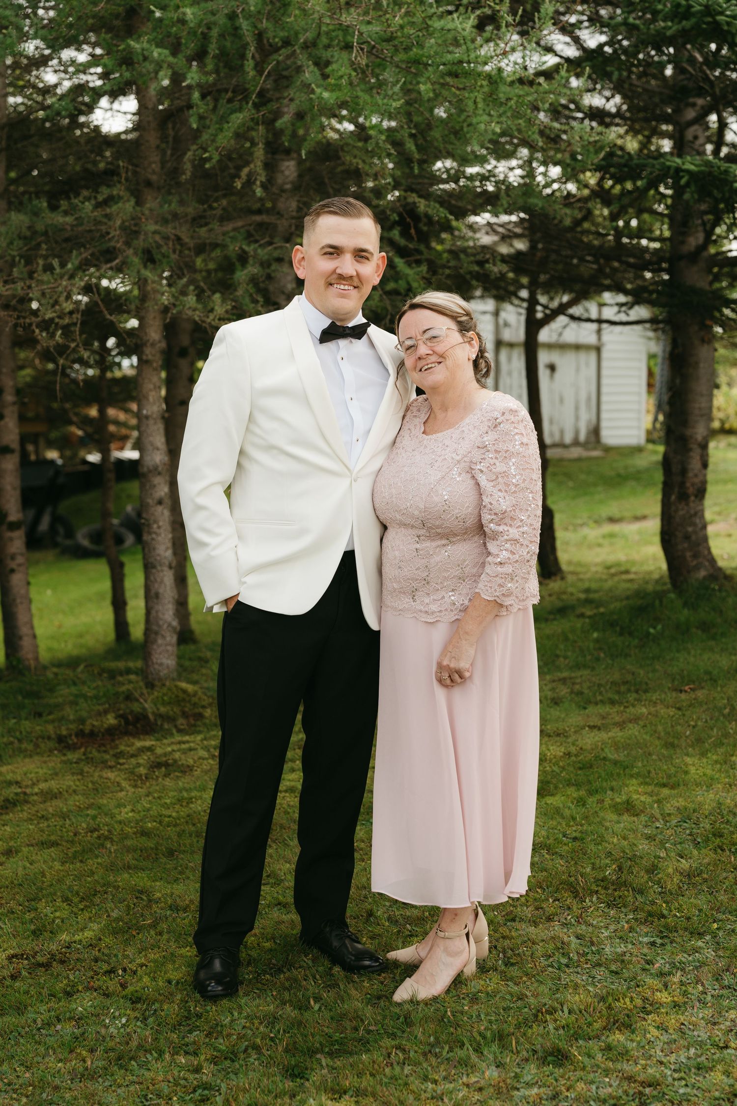 A couple in formal attire poses for romantic wedding photos in a wooded outdoor setting.