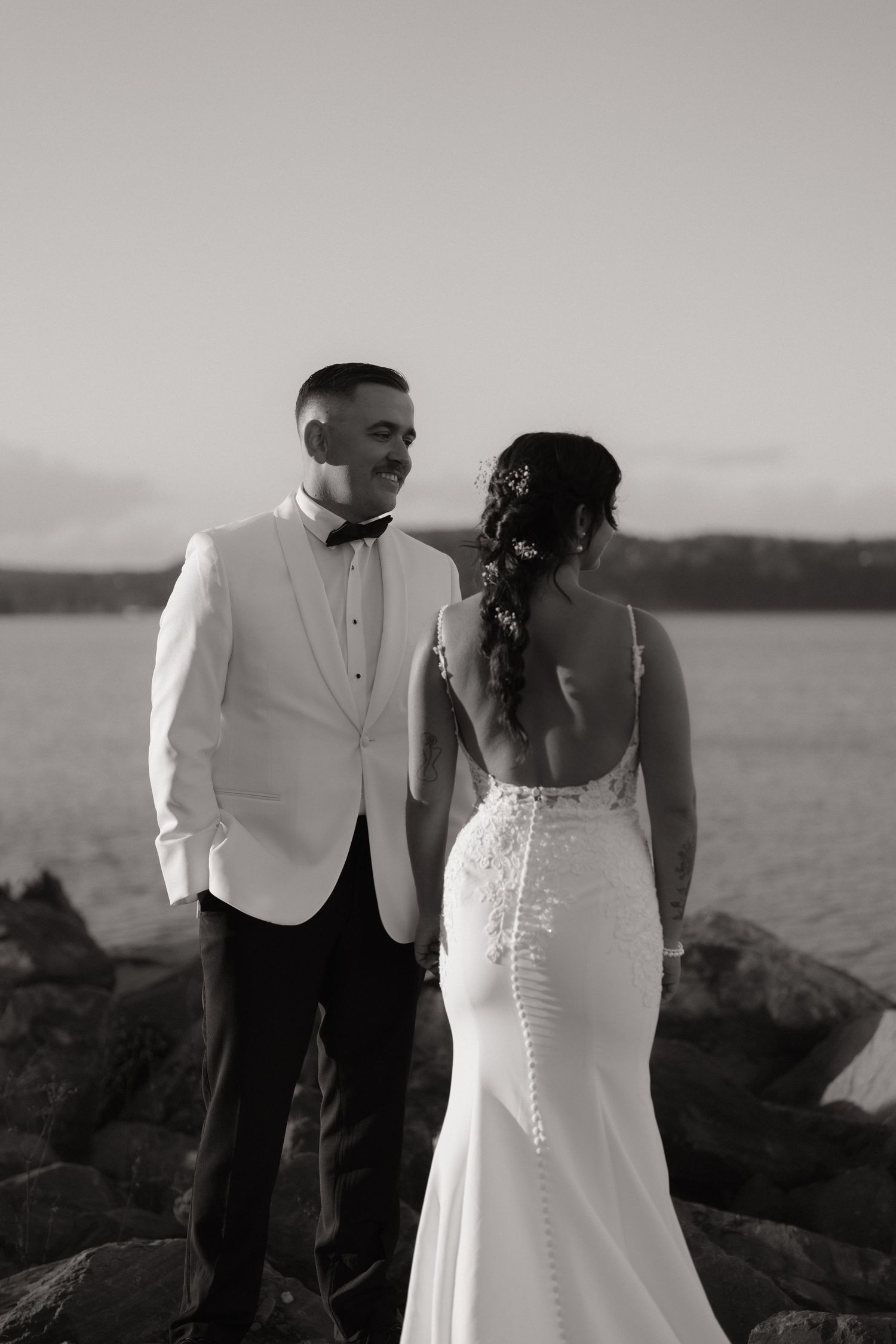 A black and white wedding photo series showing a couple on a rocky beach at sunset.
