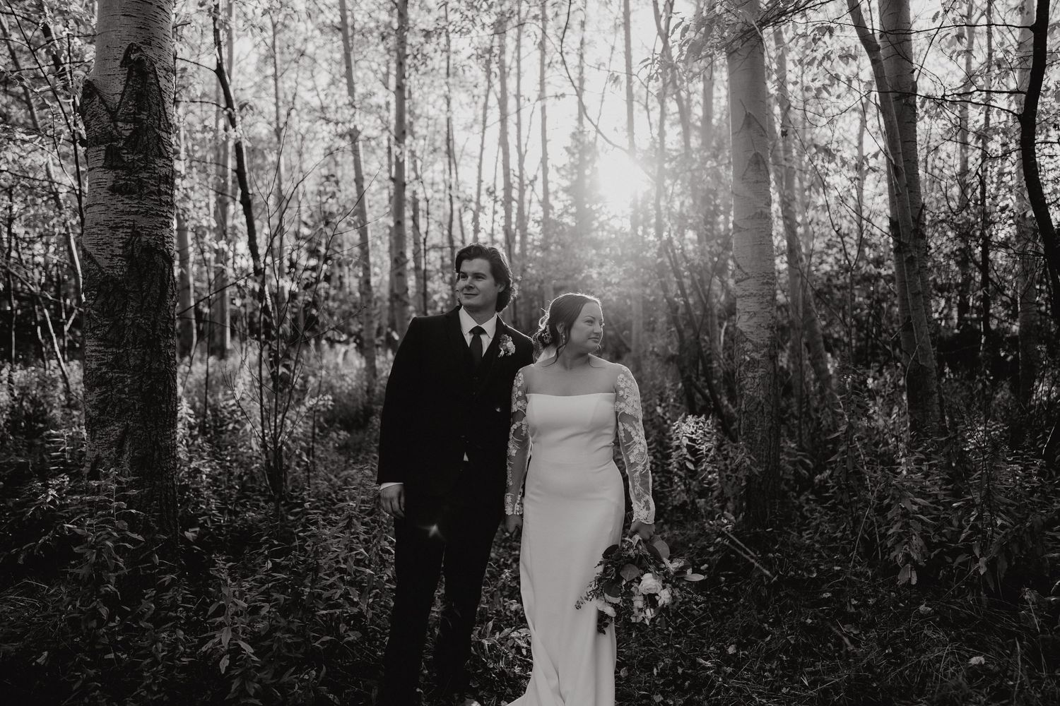 Black and white photo of newlyweds in a sunlit forest setting.