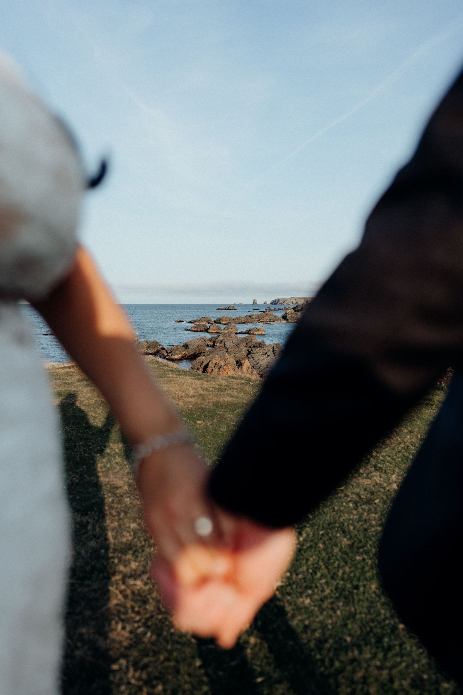 Couple holding hands with blurred coastal landscape in background during sunset.