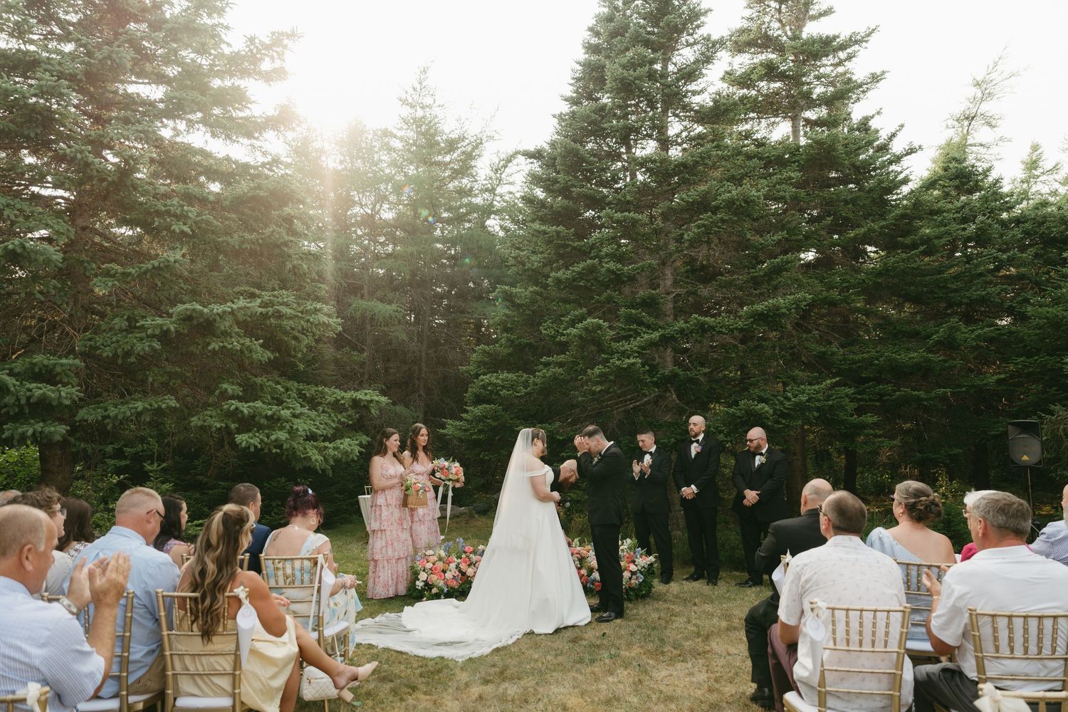 Sunset wedding ceremony in progress with pine trees and white chairs.