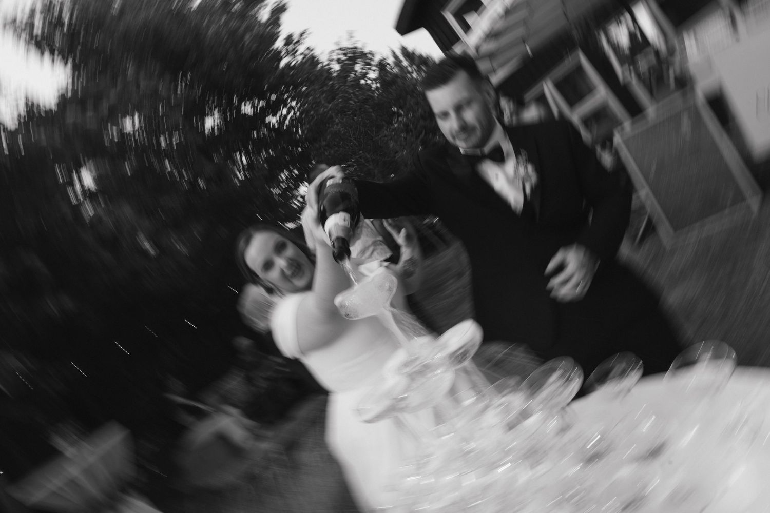 Blurred black and white image of champagne being poured at an outdoor wedding reception.