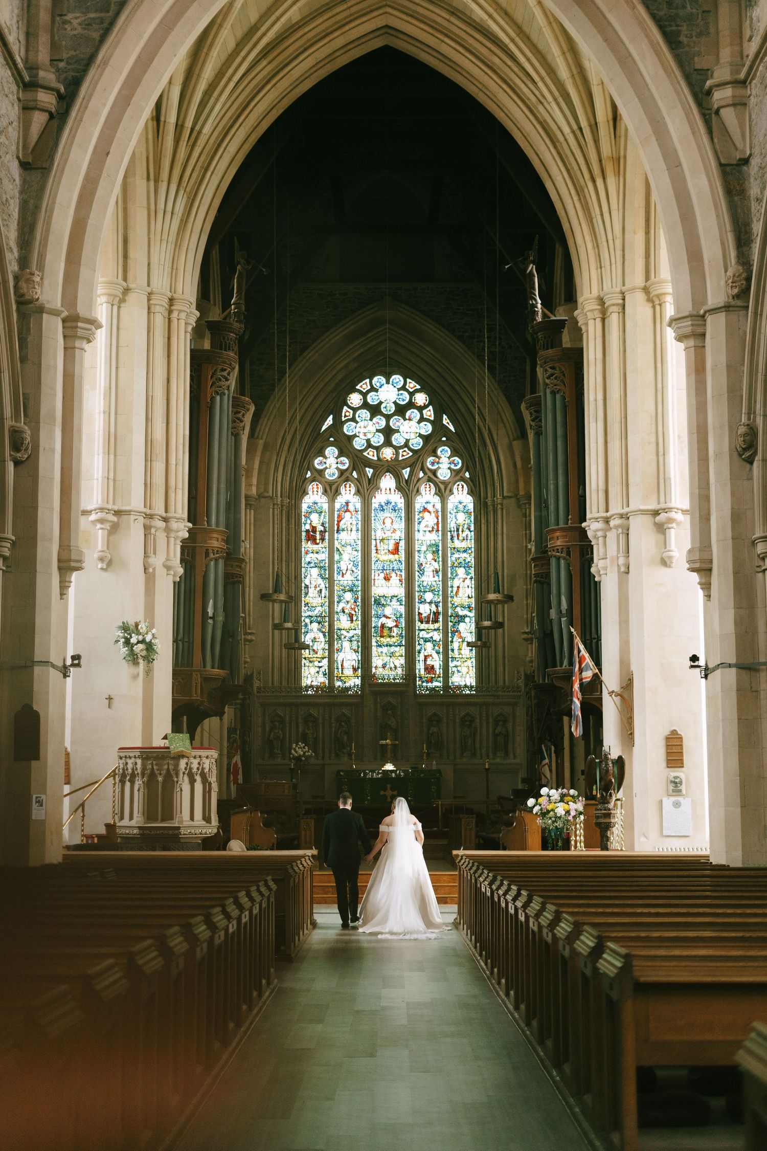 Cathedral interior wedding photos showing a dramatic view down the aisle with stained glass windows.