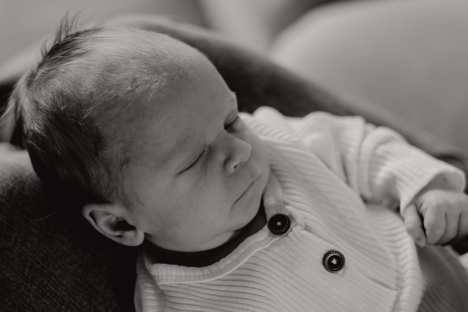 Side view of an infant sleeping peacefully in a white buttoned outfit.
