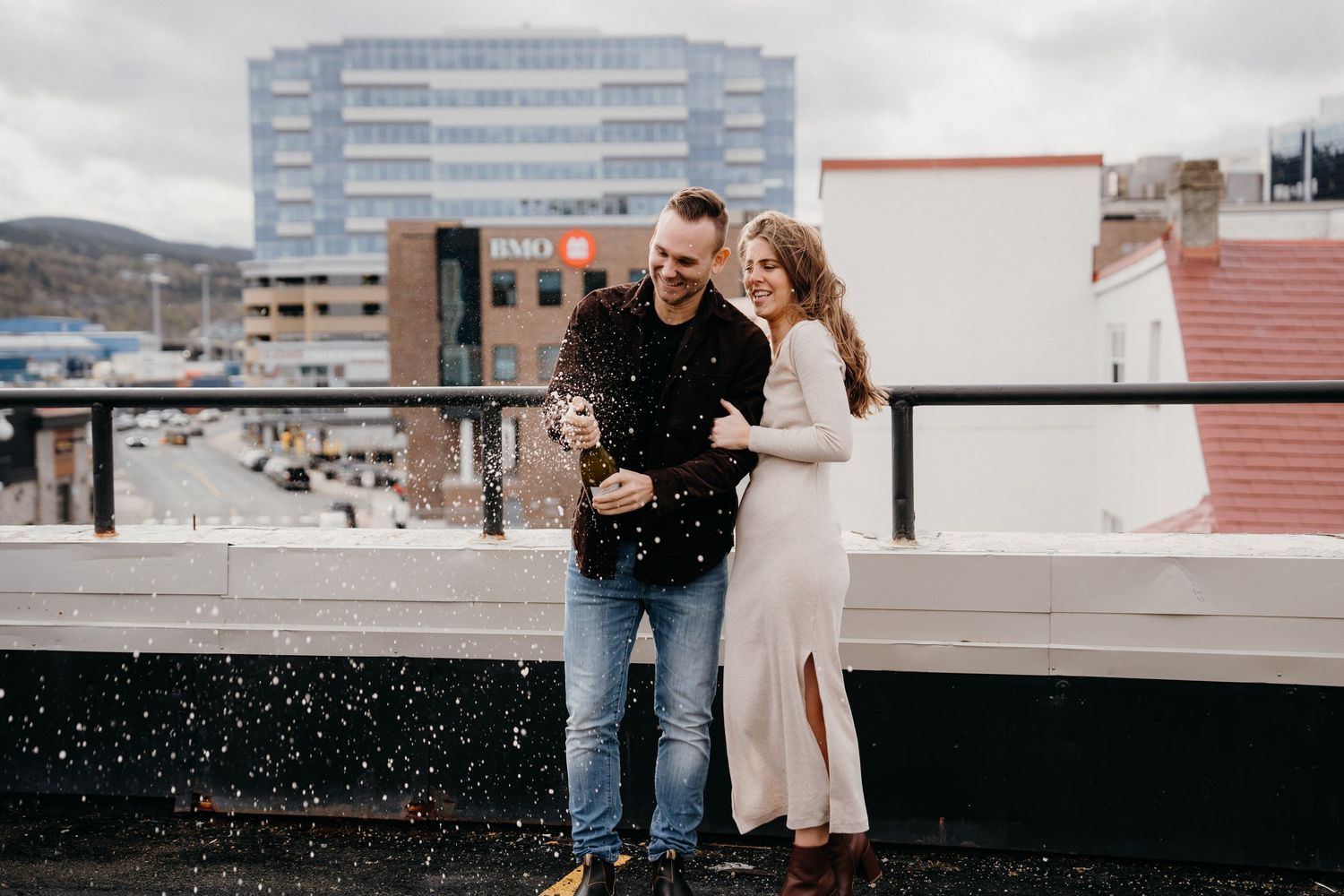 A couple shares a romantic moment on an urban rooftop with city buildings in the background.