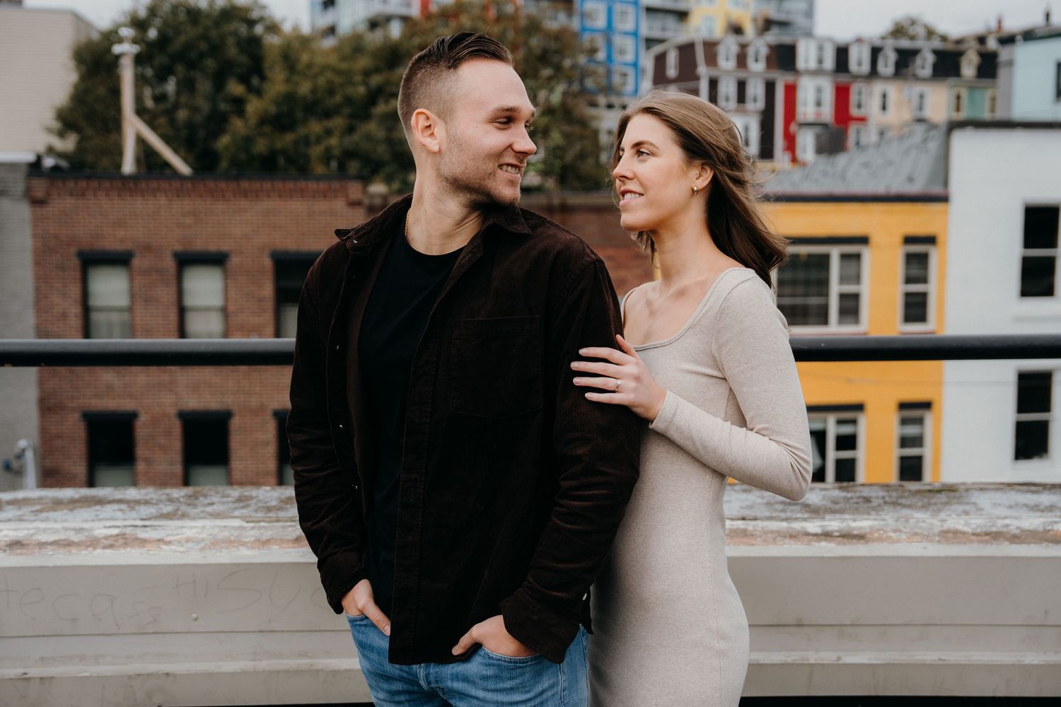 Romantic couple strolling together on a rooftop parking area with city buildings in background.