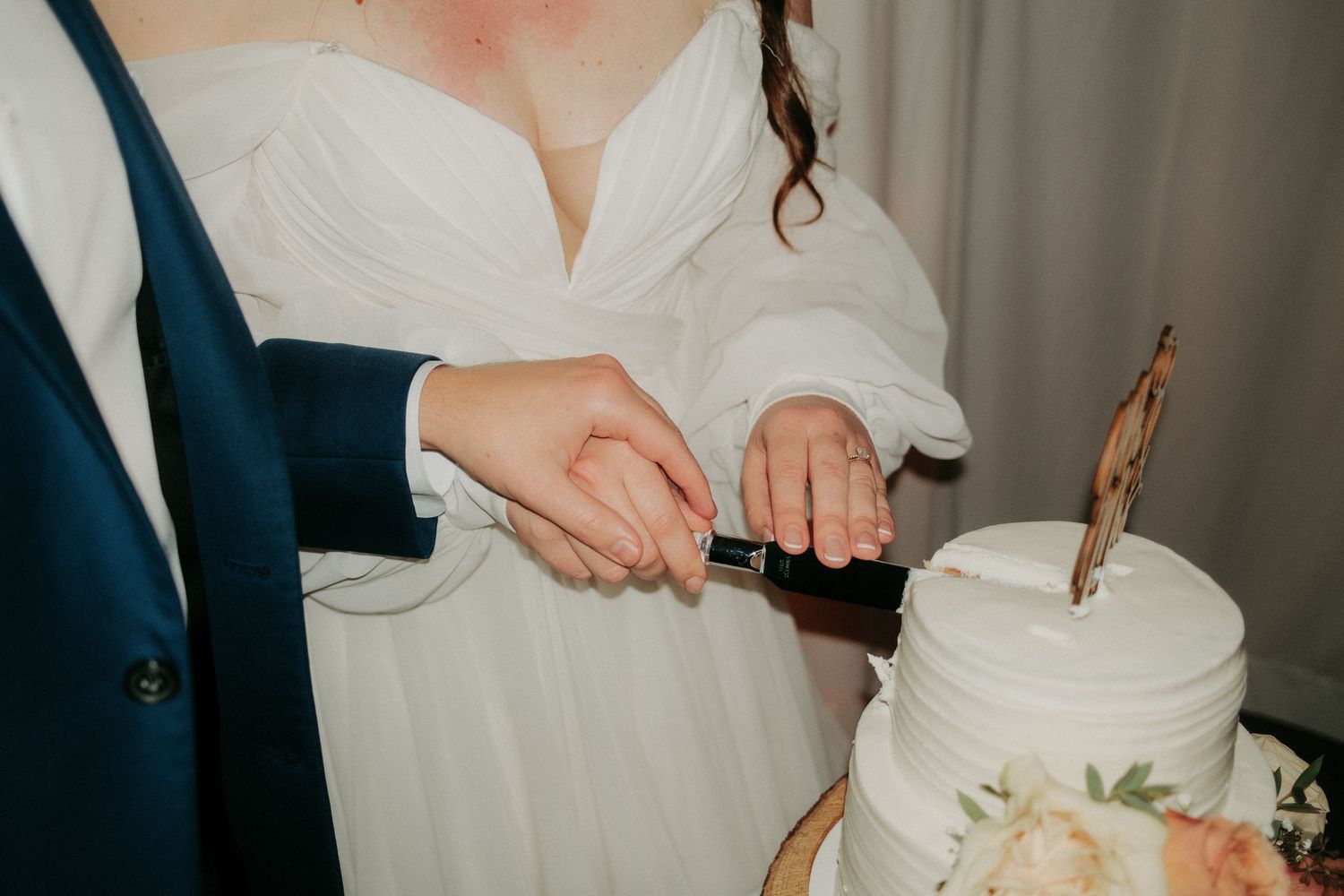 Close-up view of a couple cutting their wedding cake together with hands intertwined on the knife.