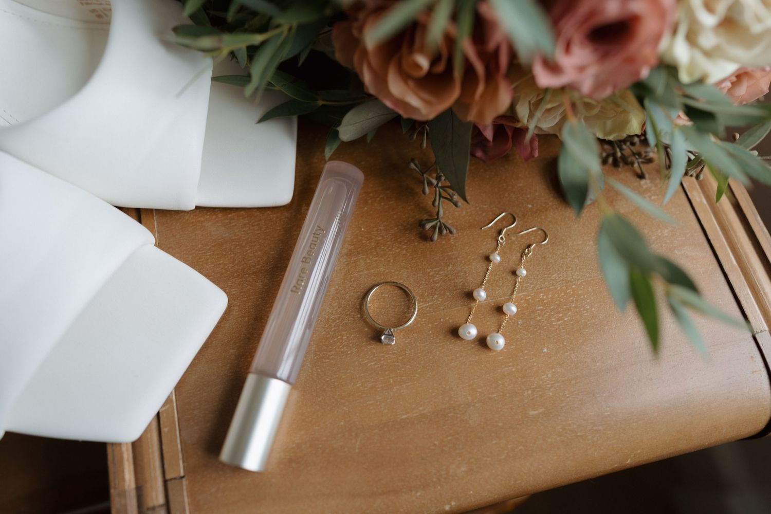 Wedding rings and delicate floral arrangements with blush roses and greenery styled on a wooden surface.