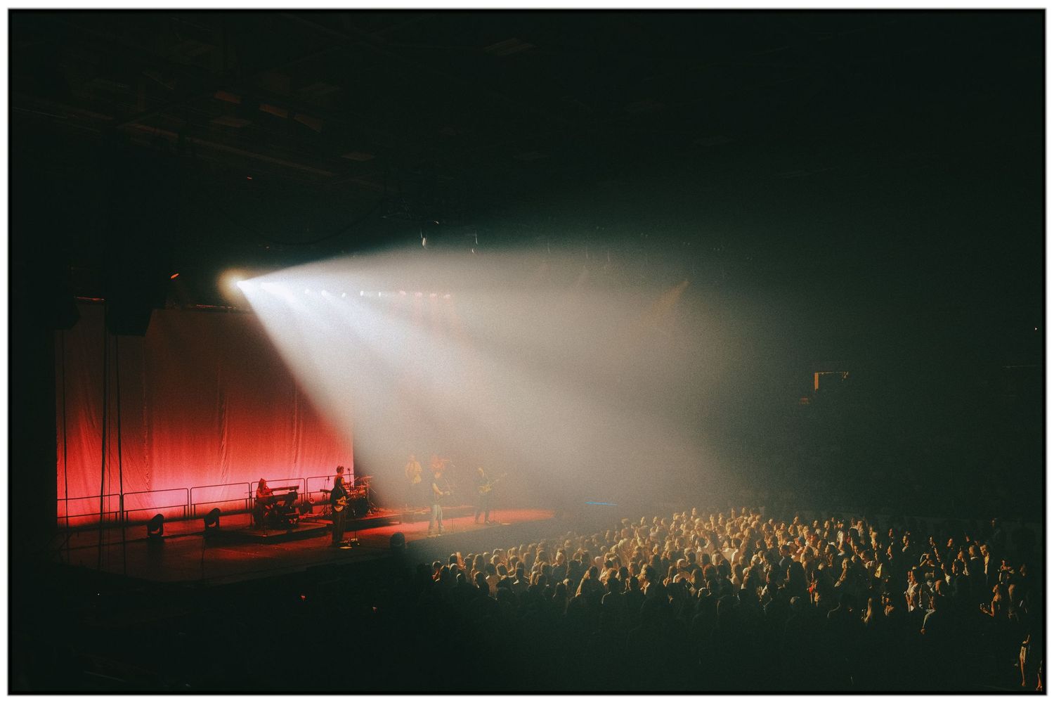 Silhouettes of concert crowd and stage lighting create a dramatic atmosphere during a live music performance.