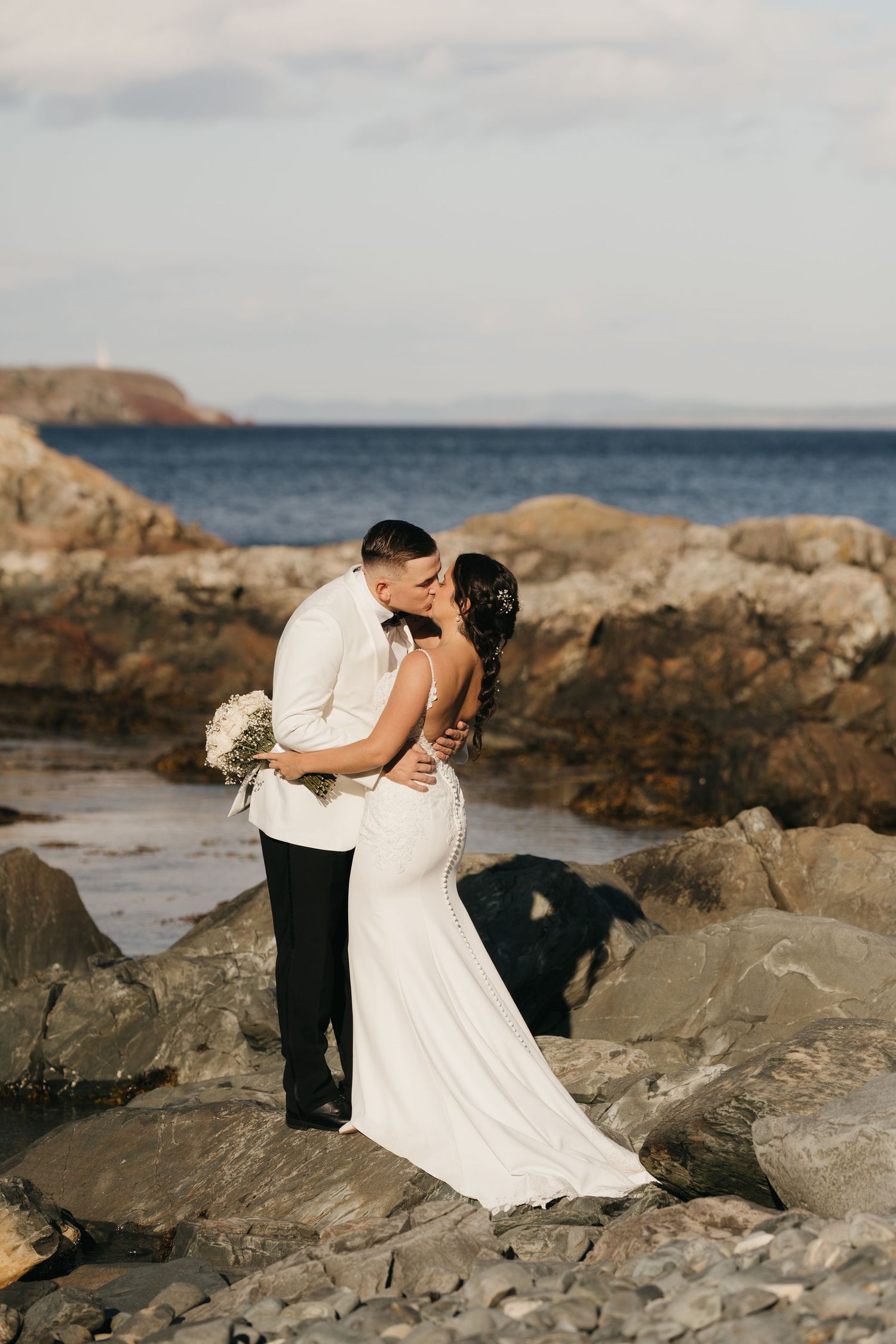 A romantic coastal wedding photo session on rocky cliffs overlooking the ocean at sunset.
