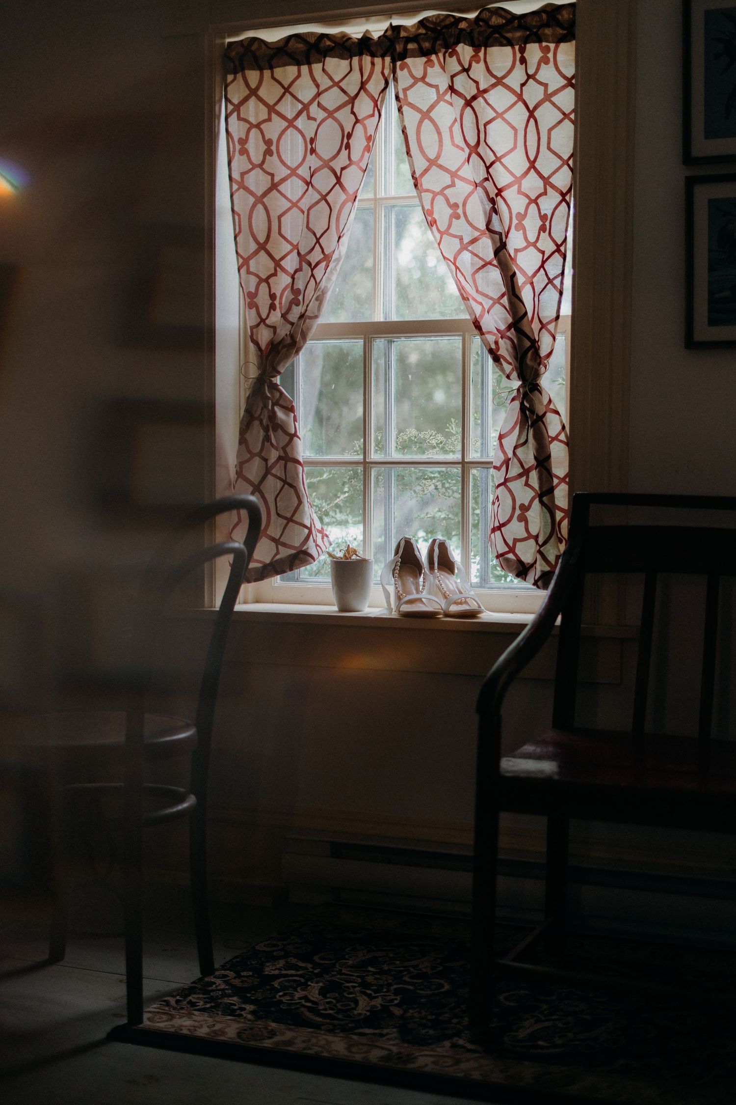 Moody interior scene with red patterned curtains framing windows, creating dramatic shadows and lighting.