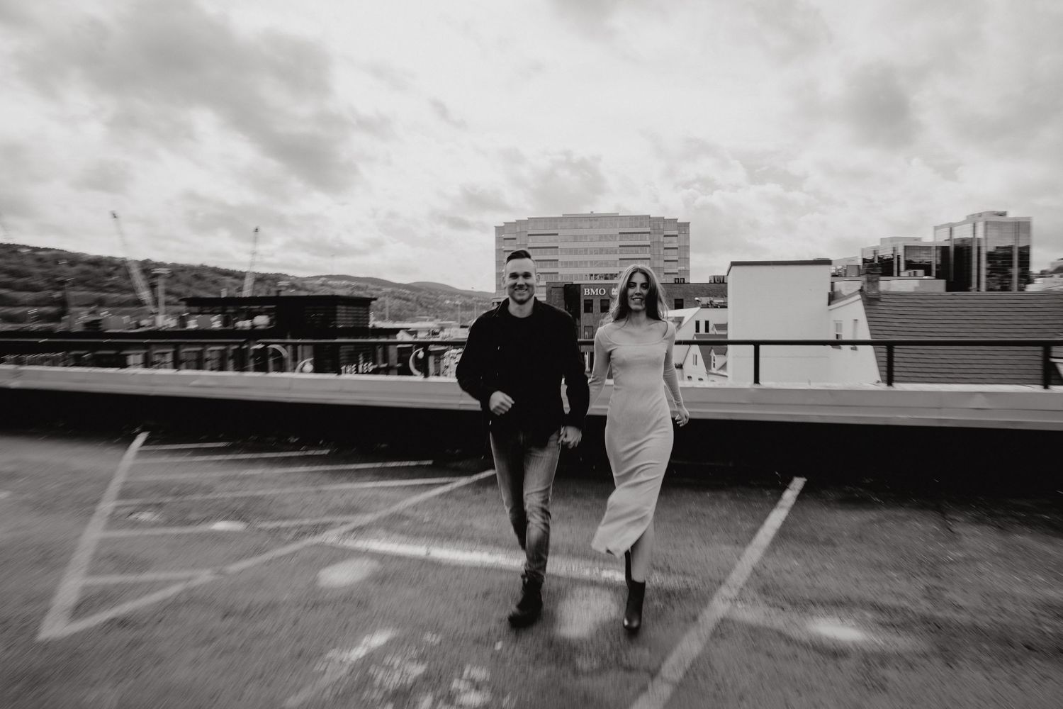 Black and white photo of a couple standing together on an urban rooftop with downtown buildings visible.