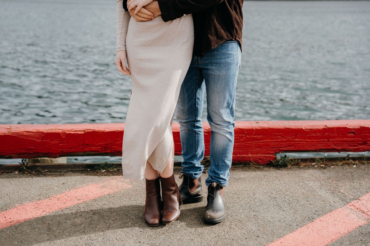 A romantic waterside photo featuring a white dress and casual attire against a red-painted walkway.