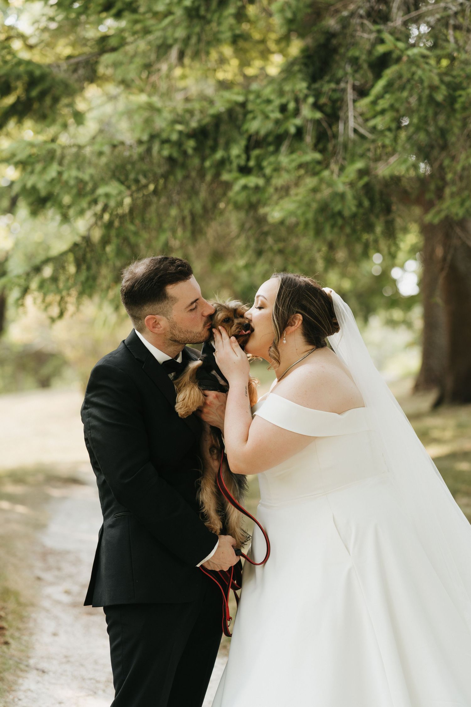 Wedding couple shares joyful moments with their small dog in an outdoor garden setting.