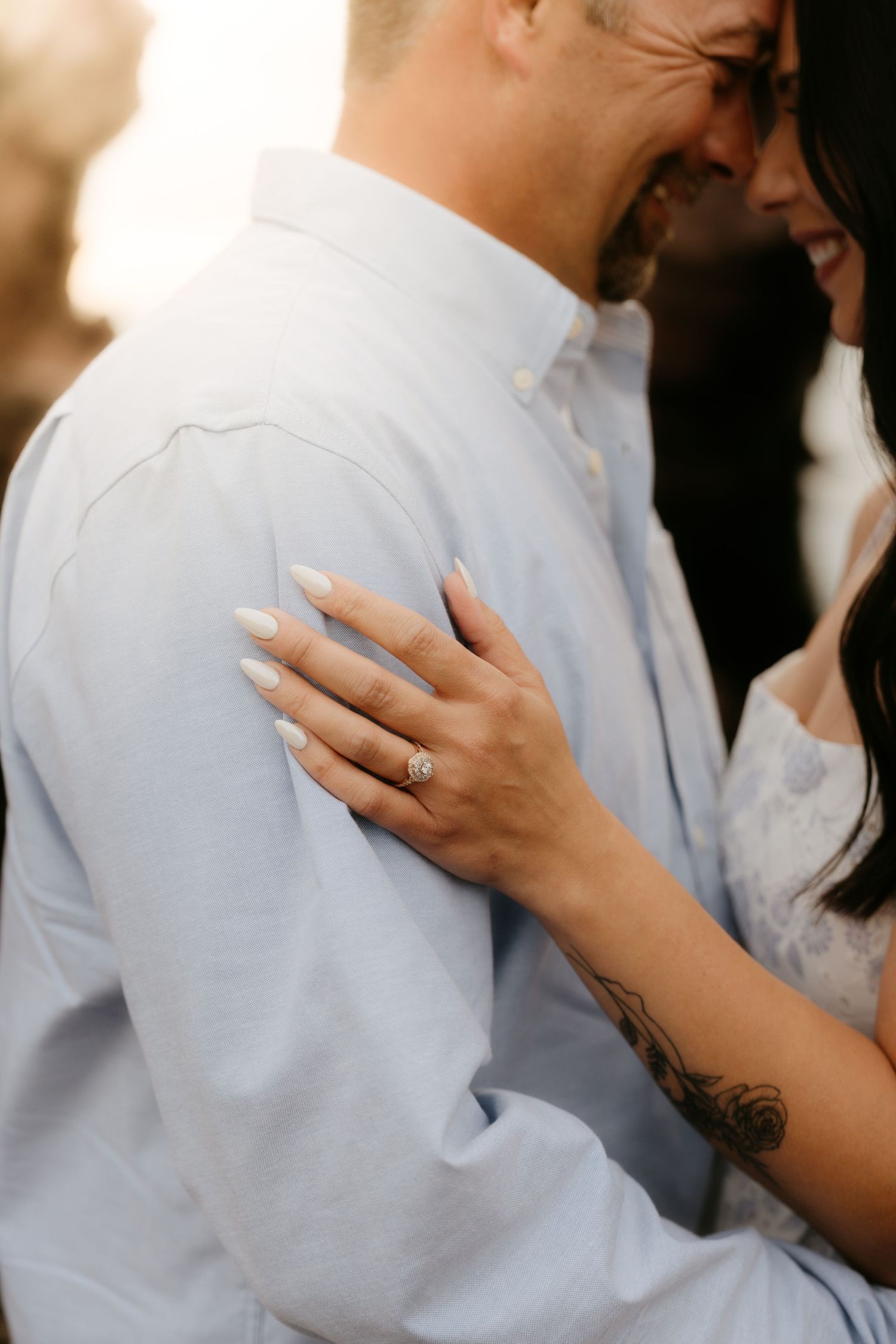 Close-up of a woman's hand with an engagement ring resting on a man's shoulder during a romantic couples photo session.