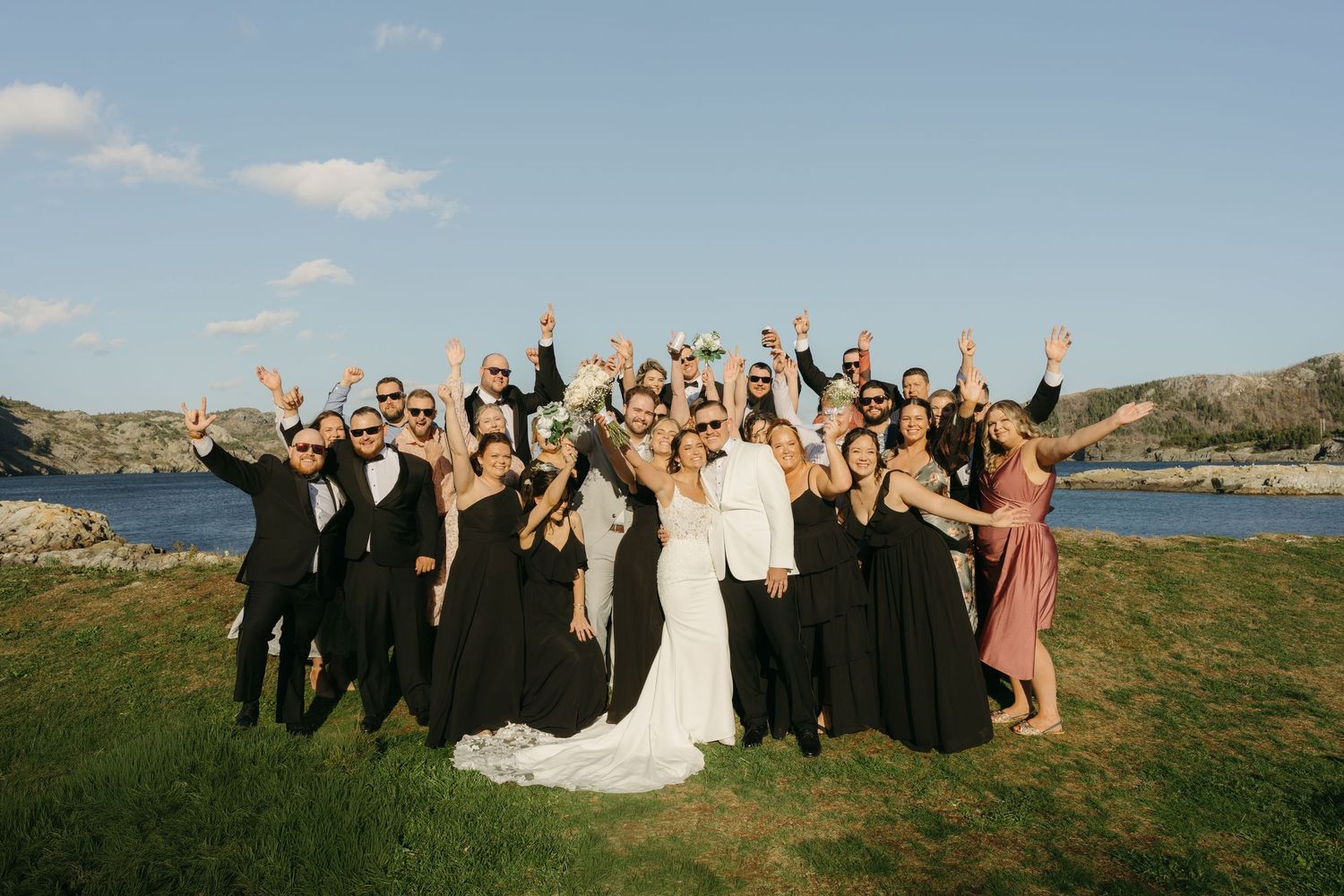 Wedding party celebrates with raised arms against scenic mountain backdrop during outdoor ceremony.