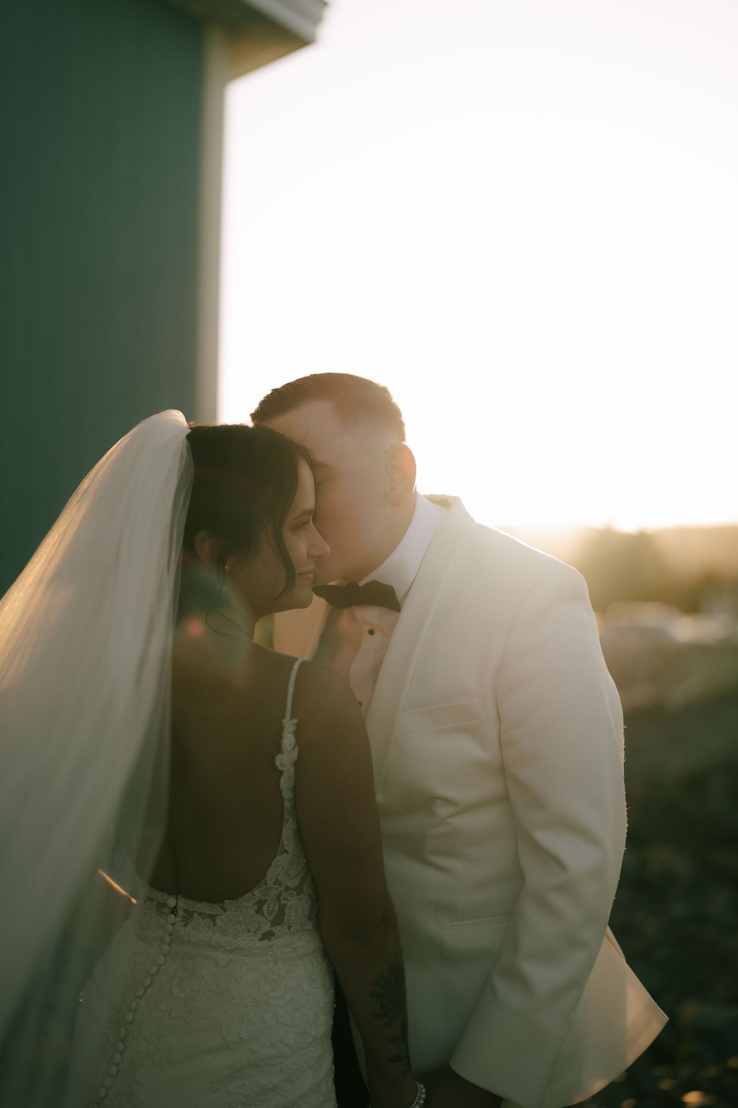 A romantic wedding couple shares an intimate moment at sunset, with soft light creating a dreamy silhouette effect.