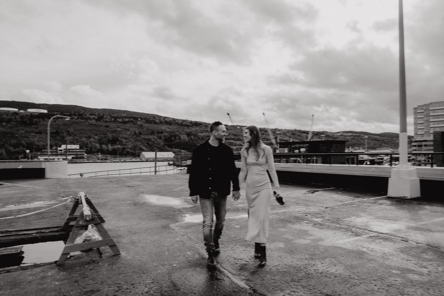 A couple walking together on a wet concrete surface with cloudy skies in the background.