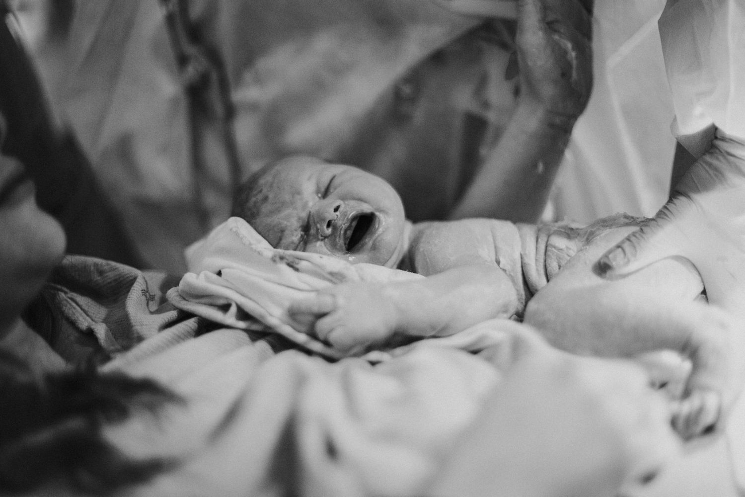 A sleeping newborn baby swaddled in soft white blankets during a lifestyle photoshoot.