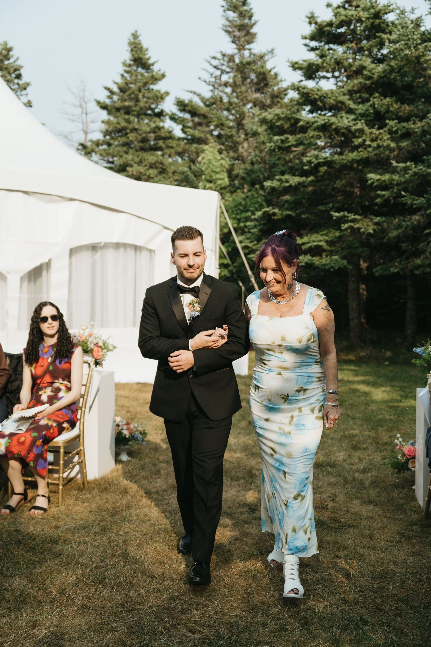 Wedding guests walking past white tents while carrying refreshments outdoors.