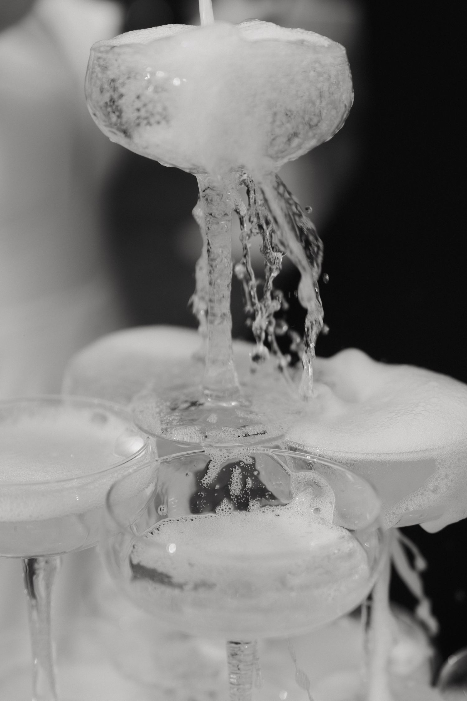 Close-up black and white shot of champagne cascading through a tower of crystal glasses.