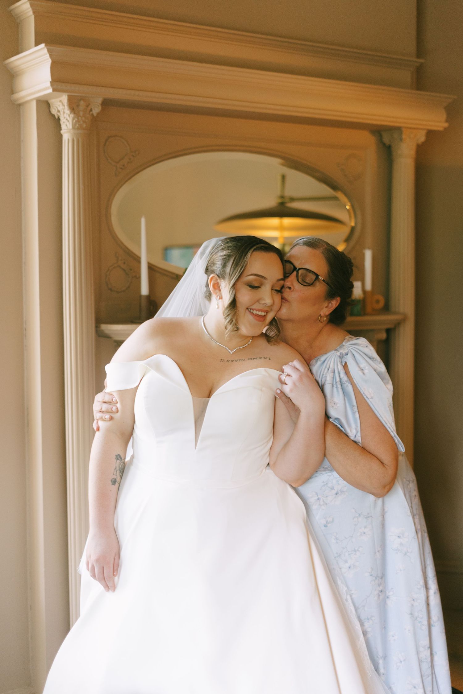 An intimate wedding moment between two people exchanging affectionate embraces in a sunlit hallway.