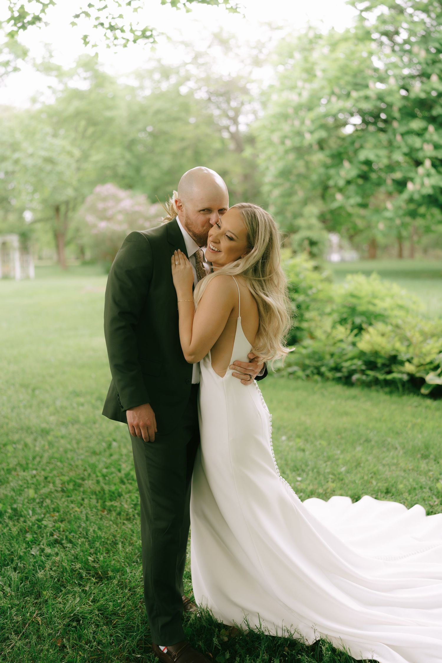 A couple shares an intimate moment in a lush green garden with a flowing white wedding dress.