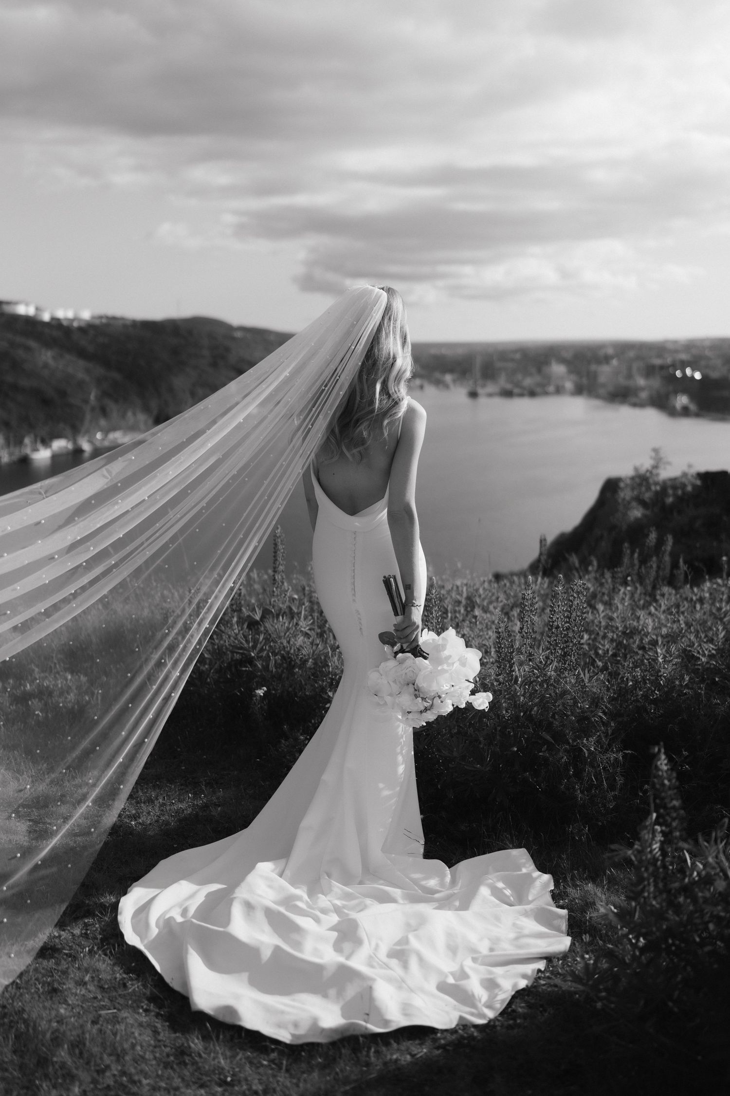Dramatic black and white bridal portrait with flowing veil against seaside cliffs.