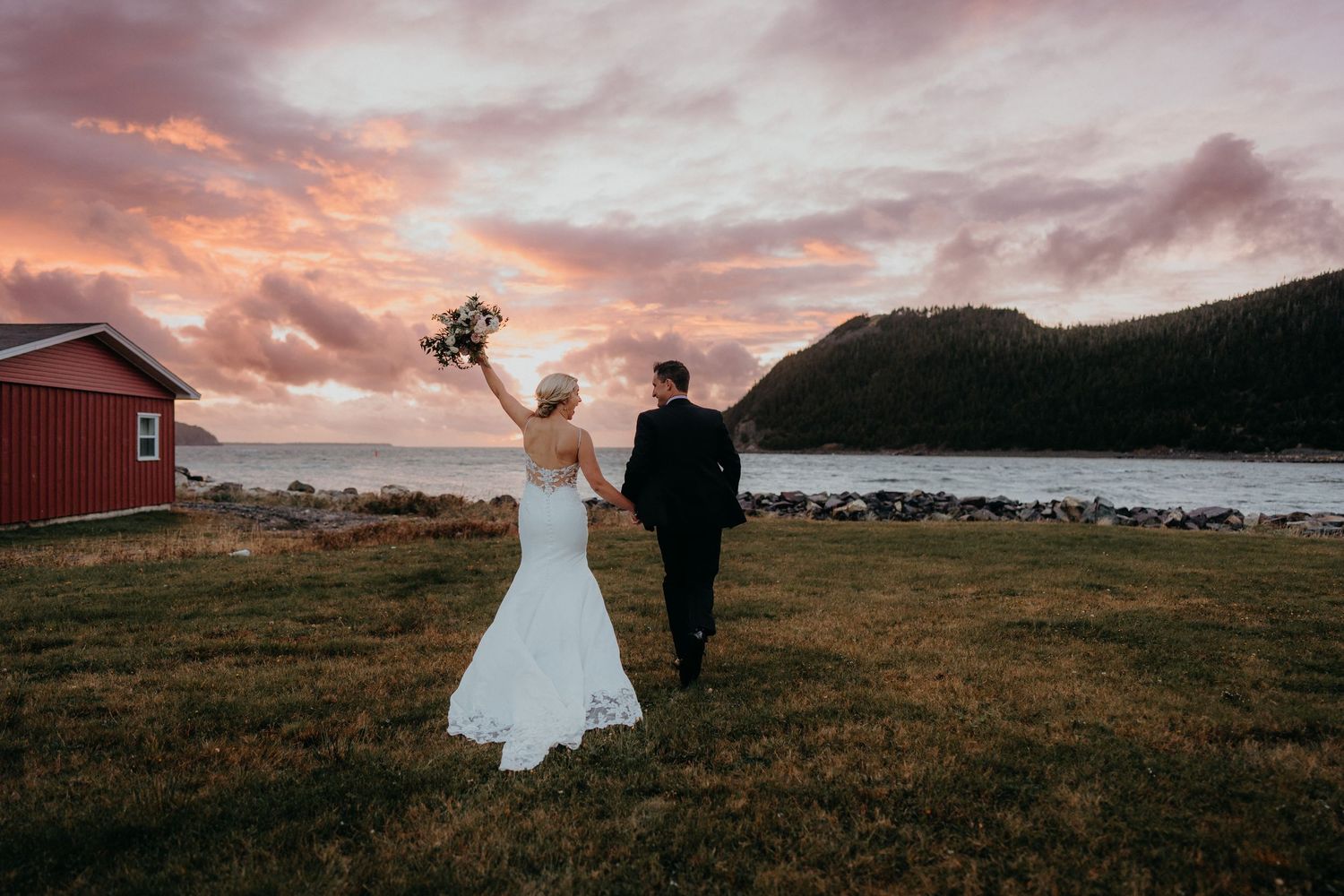Dramatic sunset wedding portraits with couple walking through coastal field.