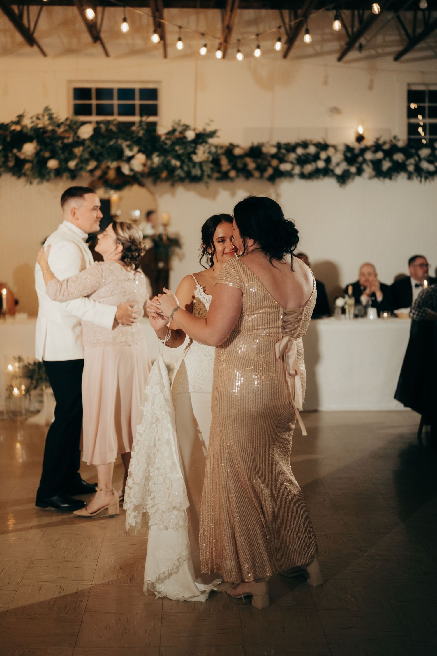 Wedding guests dancing in a dimly lit reception venue with string lights and greenery decorations overhead.