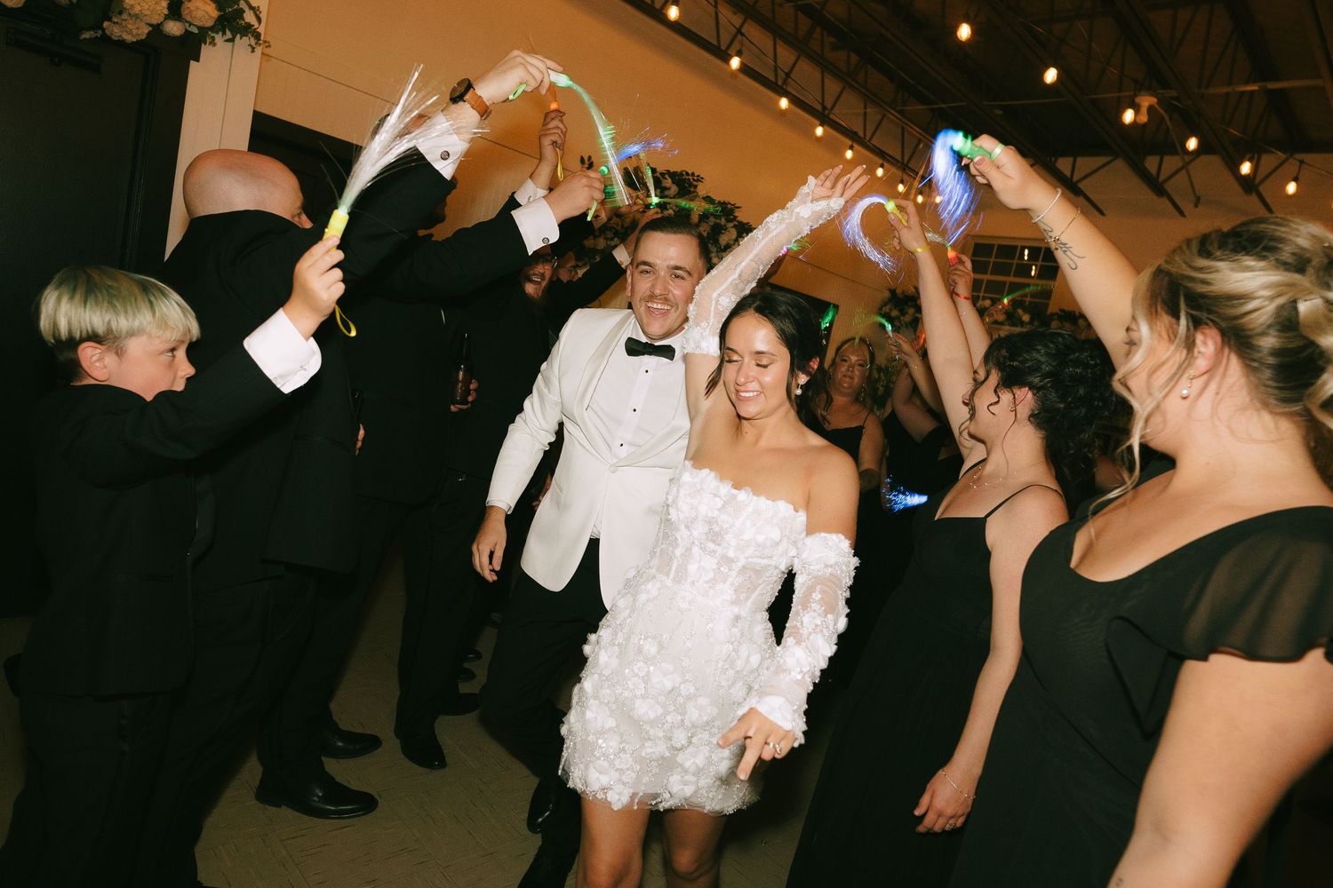 Wedding guests form a tunnel with raised arms as couple dances beneath during reception celebration.
