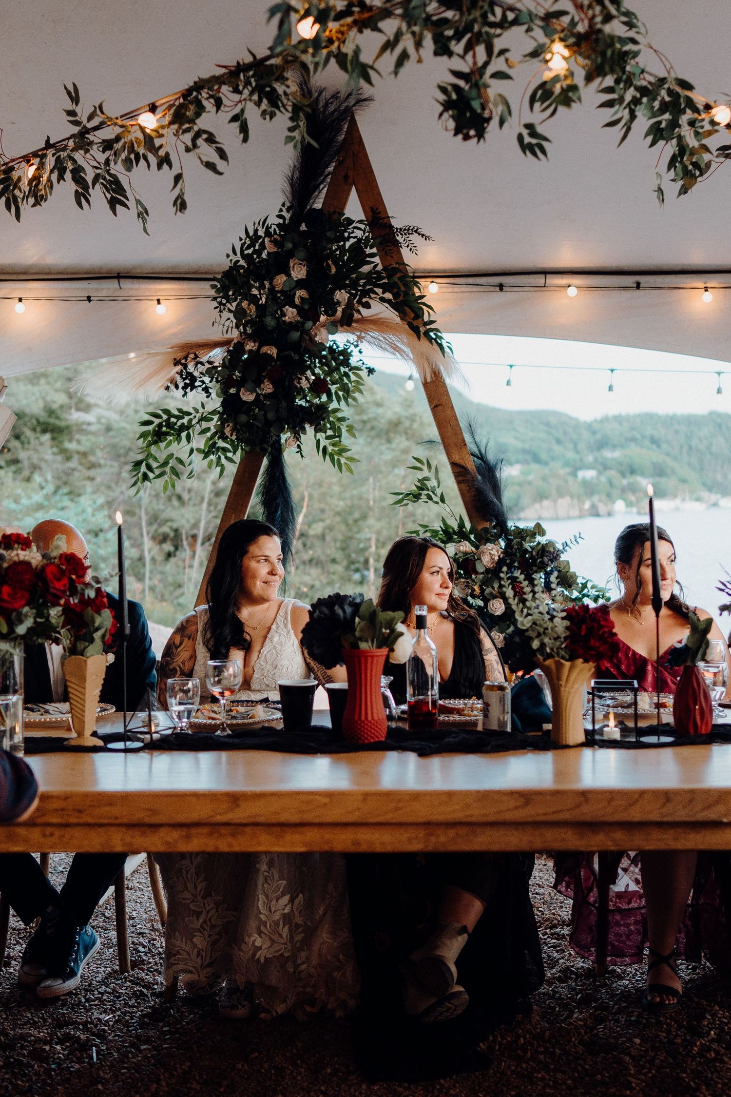 Wedding reception table under tent with string lights and greenery decorations at outdoor venue during sunset.