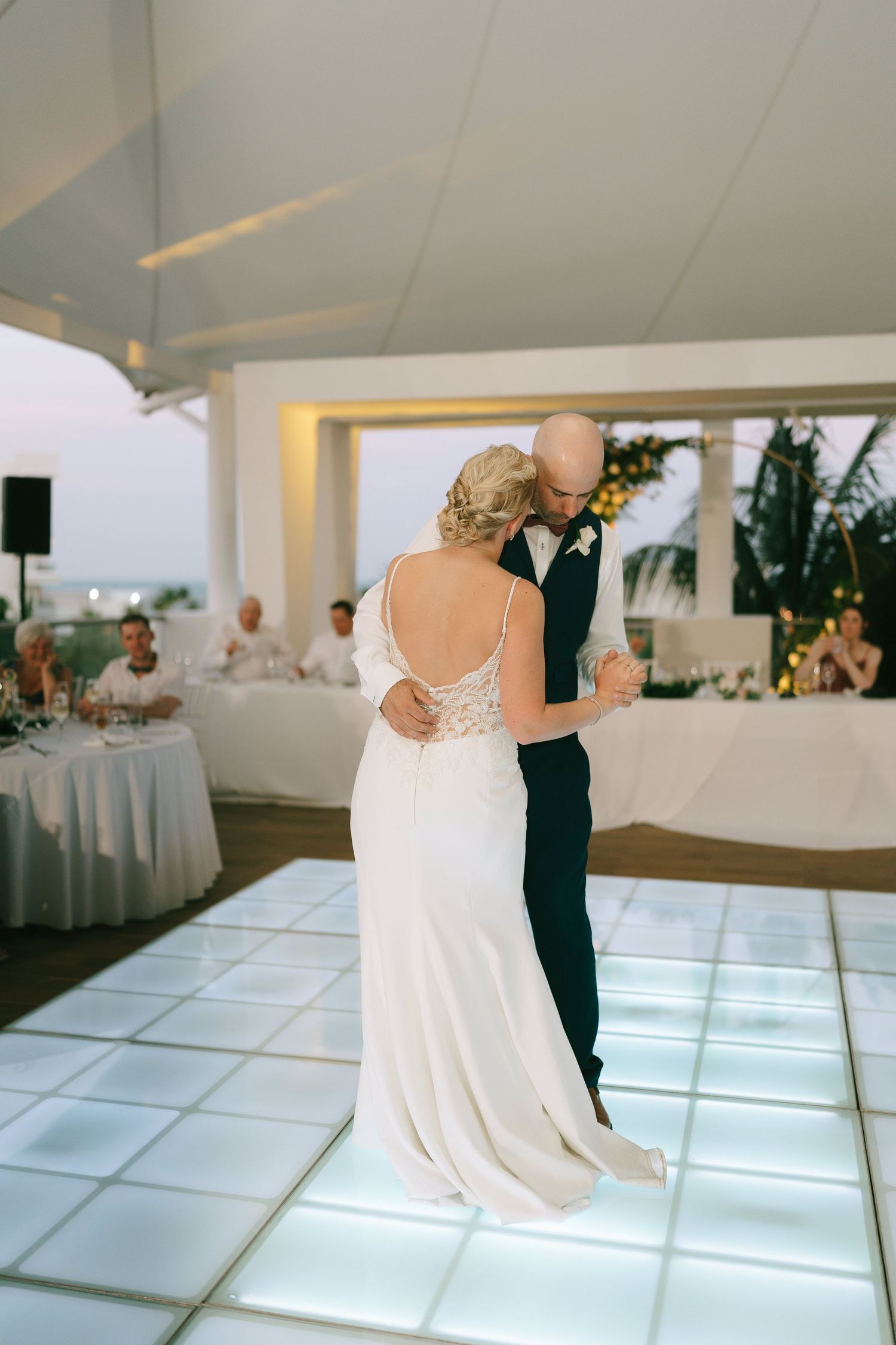 A romantic first dance on an illuminated white dance floor under an elegant reception tent.