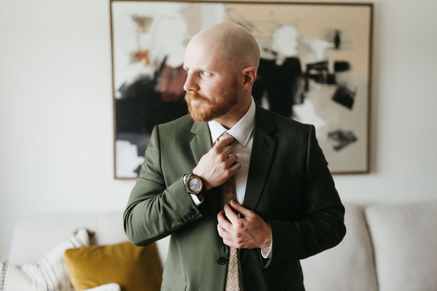 A person in a white dress shirt and dark suit jacket poses thoughtfully in an interior setting.